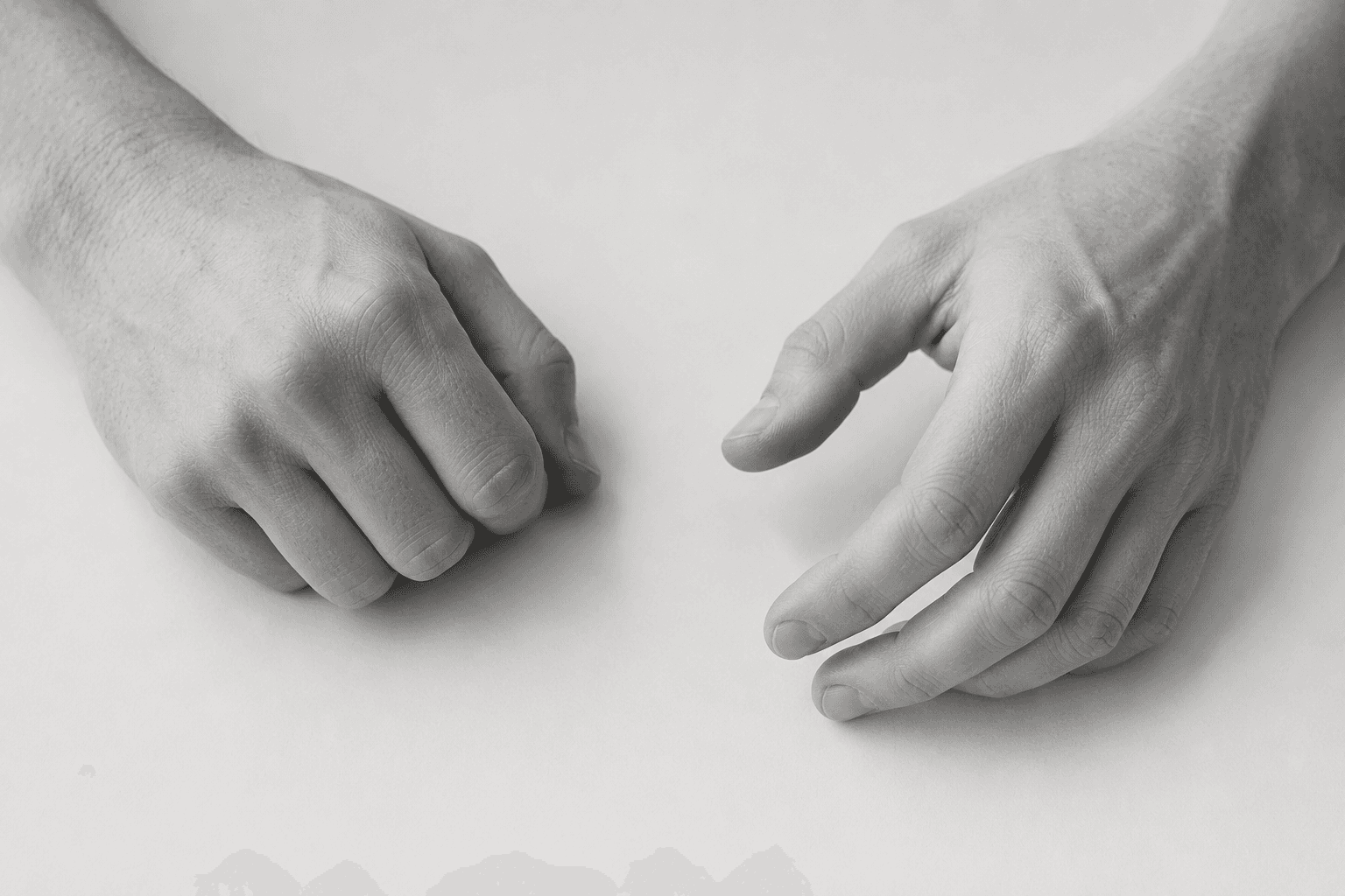 Two hands resting on a white desk evoking the quiet physical tension of chronic stress