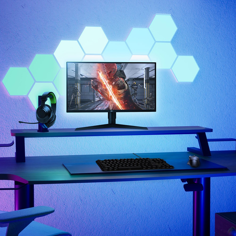 A gamer's room is illuminated by colorful lights. A computer chair, desk, speakers, monitors and few other electronics.