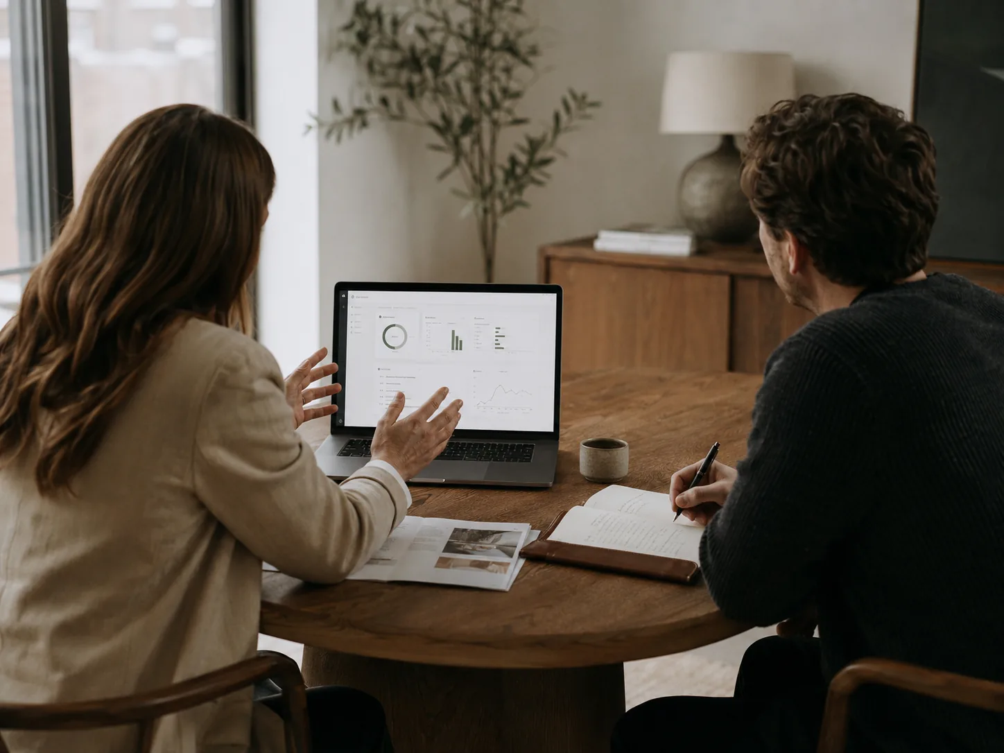 Twee professionals bekijken grafieken en gegevens op een laptop tijdens een zakelijk overleg
