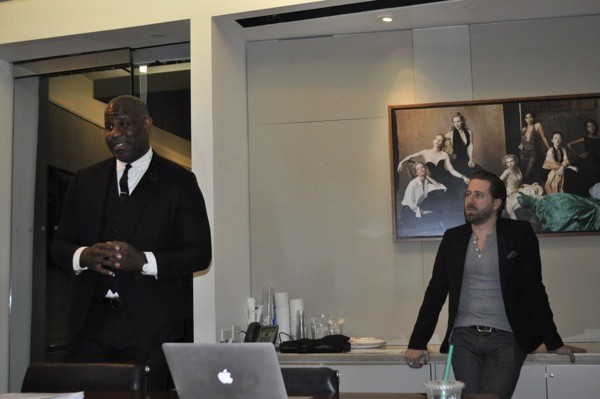 A photo of two people, one giving a lecture from a laptop and the other standing near a desk.