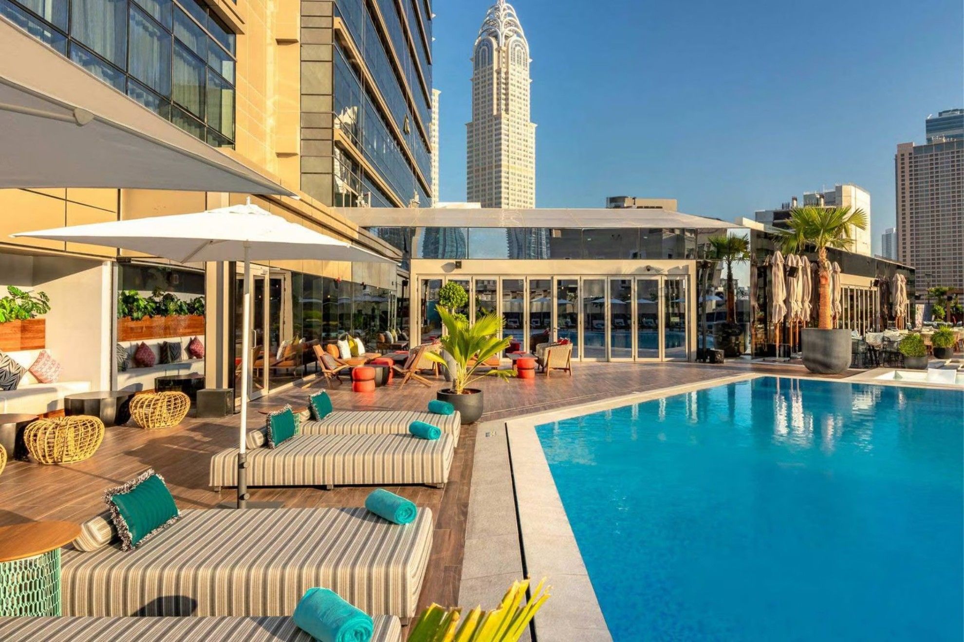 The outdoor pool of Zabeel House The Greens, featuring comfortable seating, parasols, and greenery.