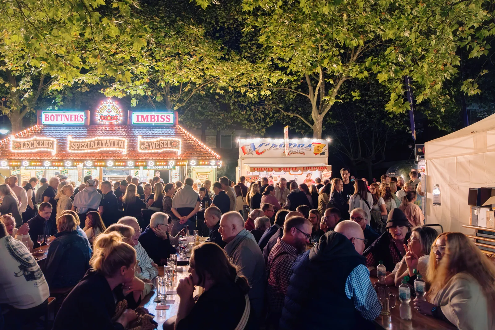 Dichtes Publikum vor der Bühne in der Dämmerung, Lichterketten über der Straße.