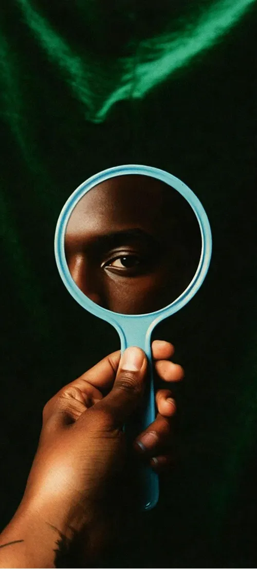 A hand holding a round mirror reflecting an eye