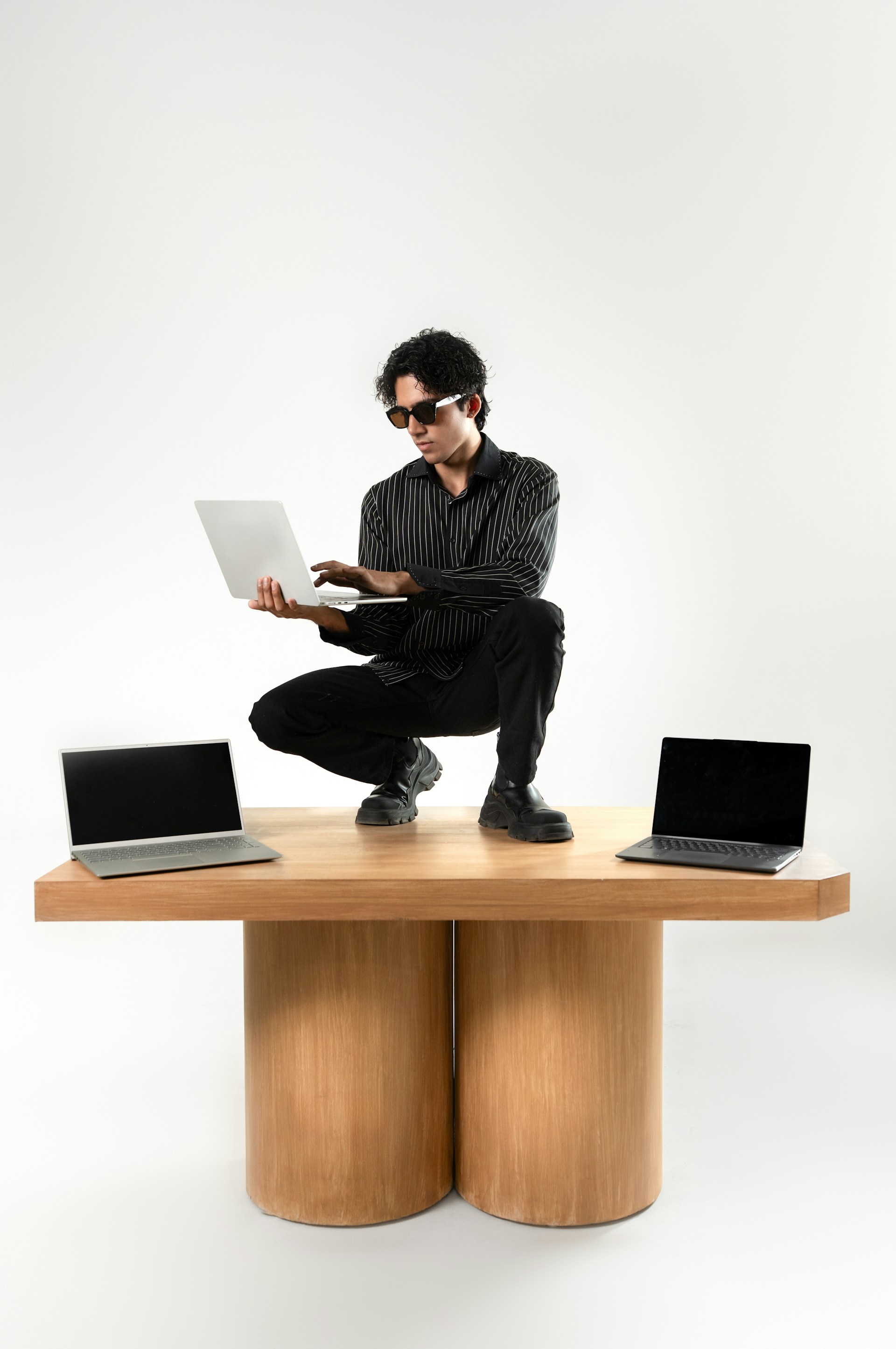 Person arbeitet mit Laptop auf Tisch zwischen zwei Laptops – kreative Arbeit und strukturierte Calls.