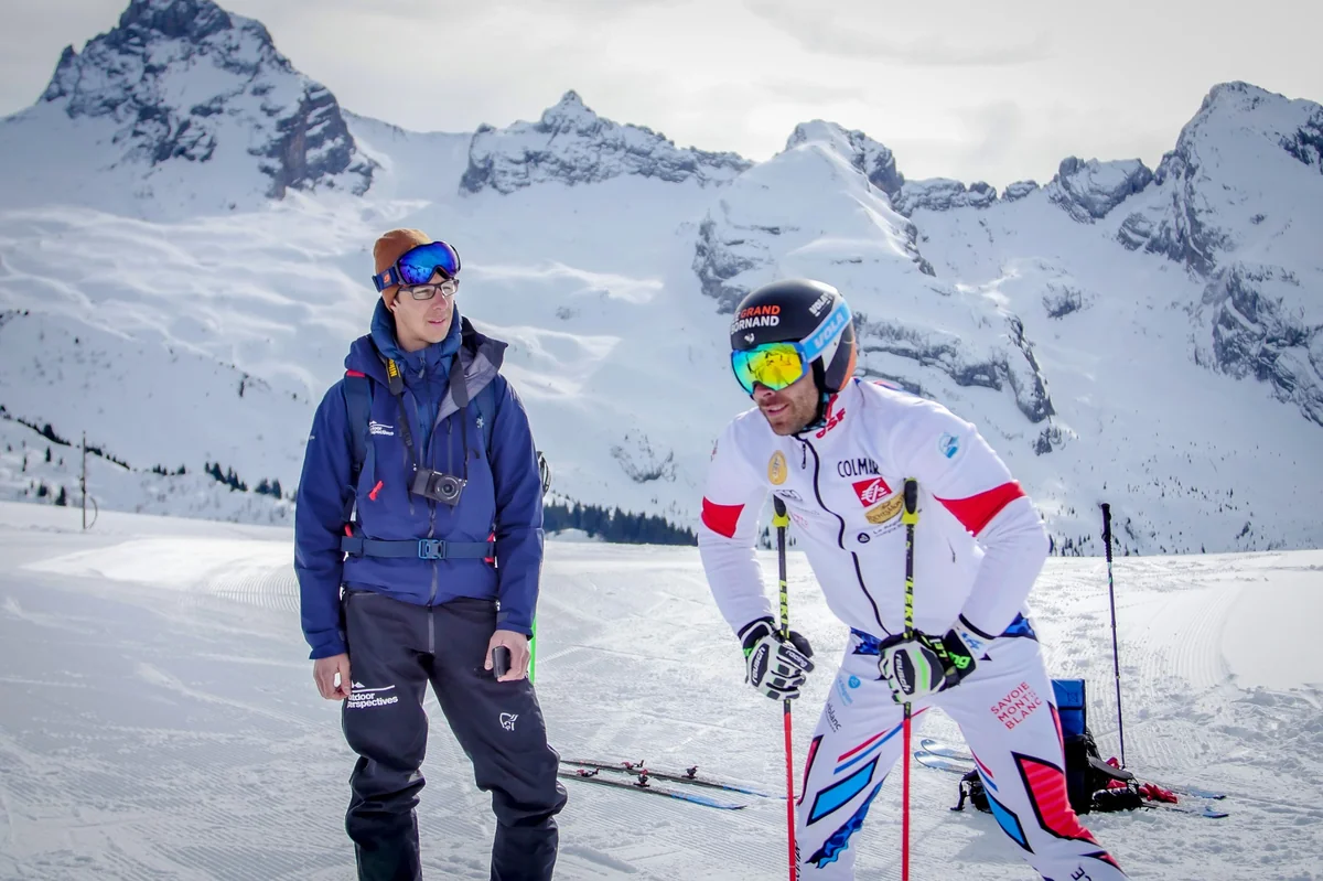 Vignette Skieur professionnel en tenue Salomon discutant avec un membre de l’équipe Outdoor Perspectives sur une piste enneigée.