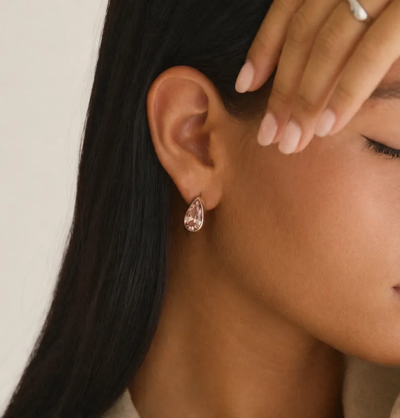 A close-up image of a person wearing a gold coin pendant earring studded with small gemstones, highlighting elegant jewelry design.