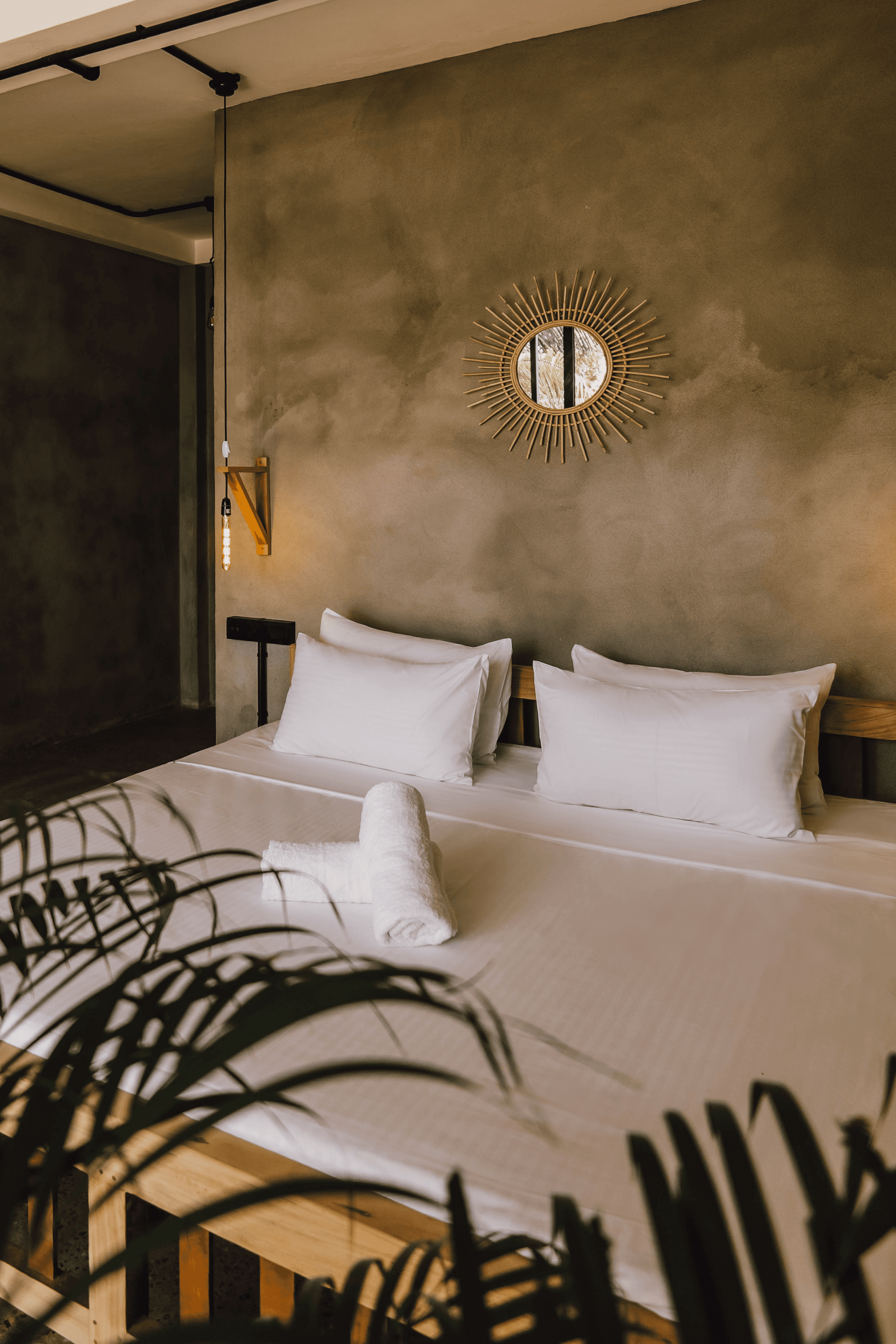 Sunburst mirror over a bed with rolled towels.
