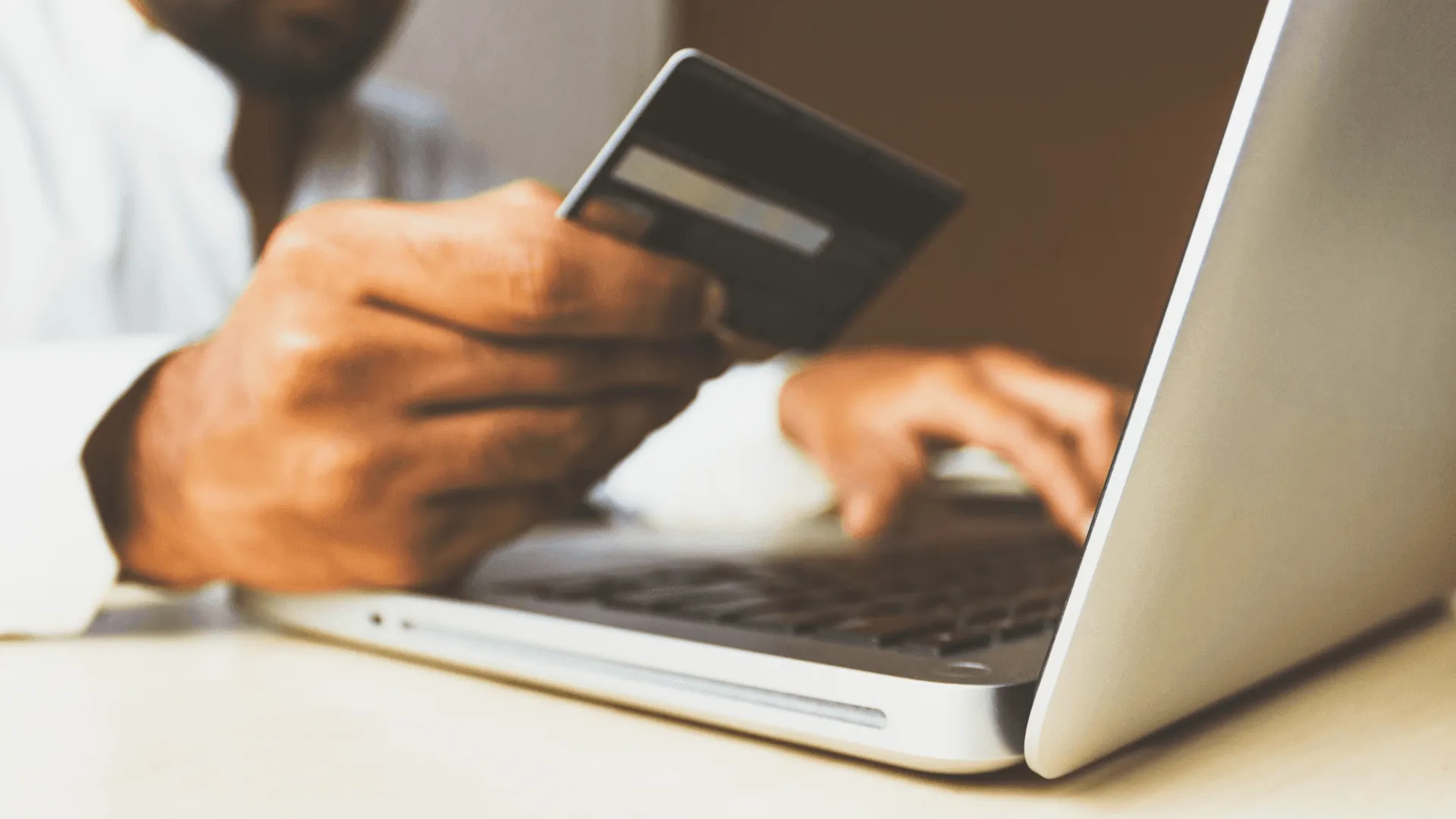 A closeup shot of a person holding a credit card while also working on a laptop giving the impression they are buying something online