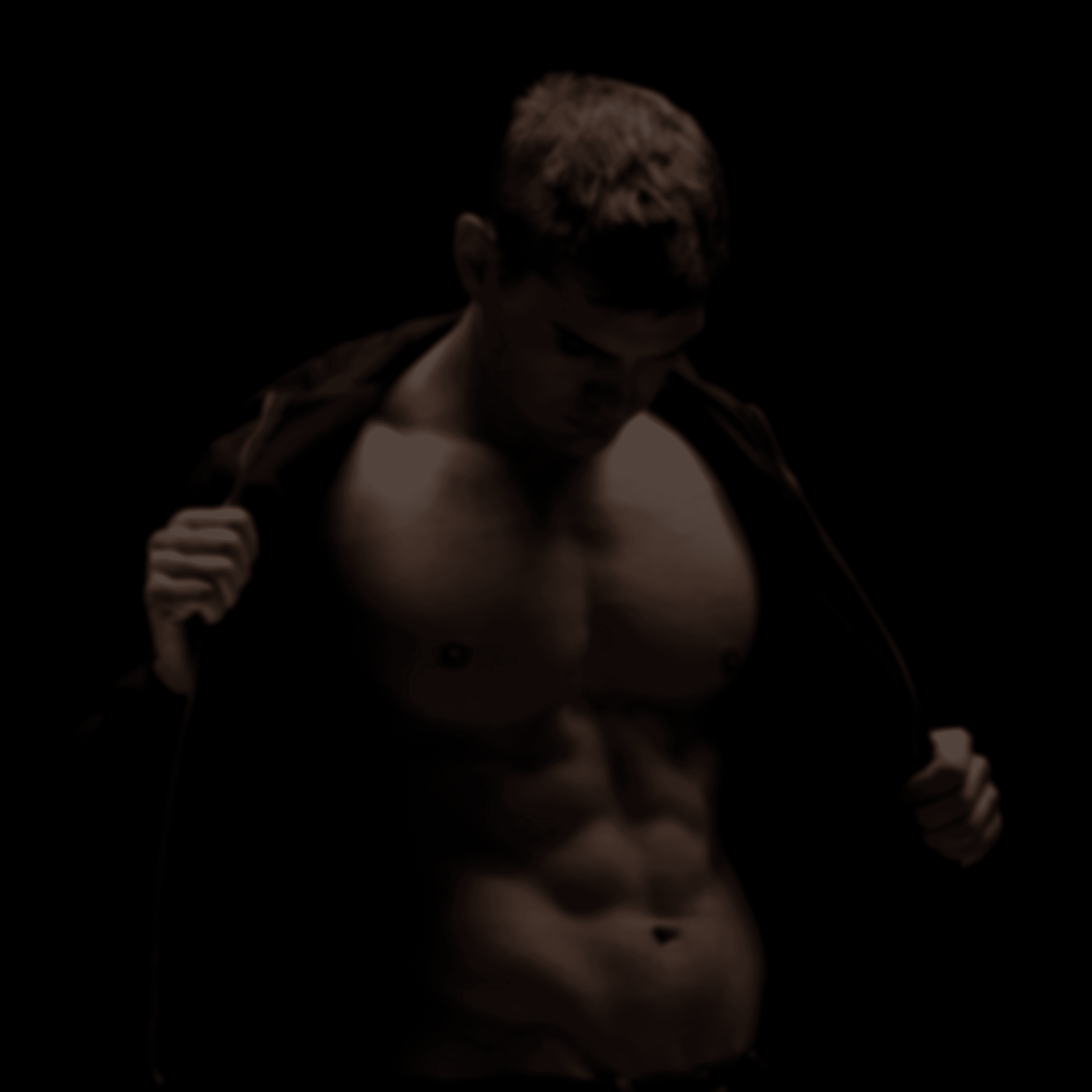 A man posing against a dark backround revealing a naked torso as he unzips his hoodie.