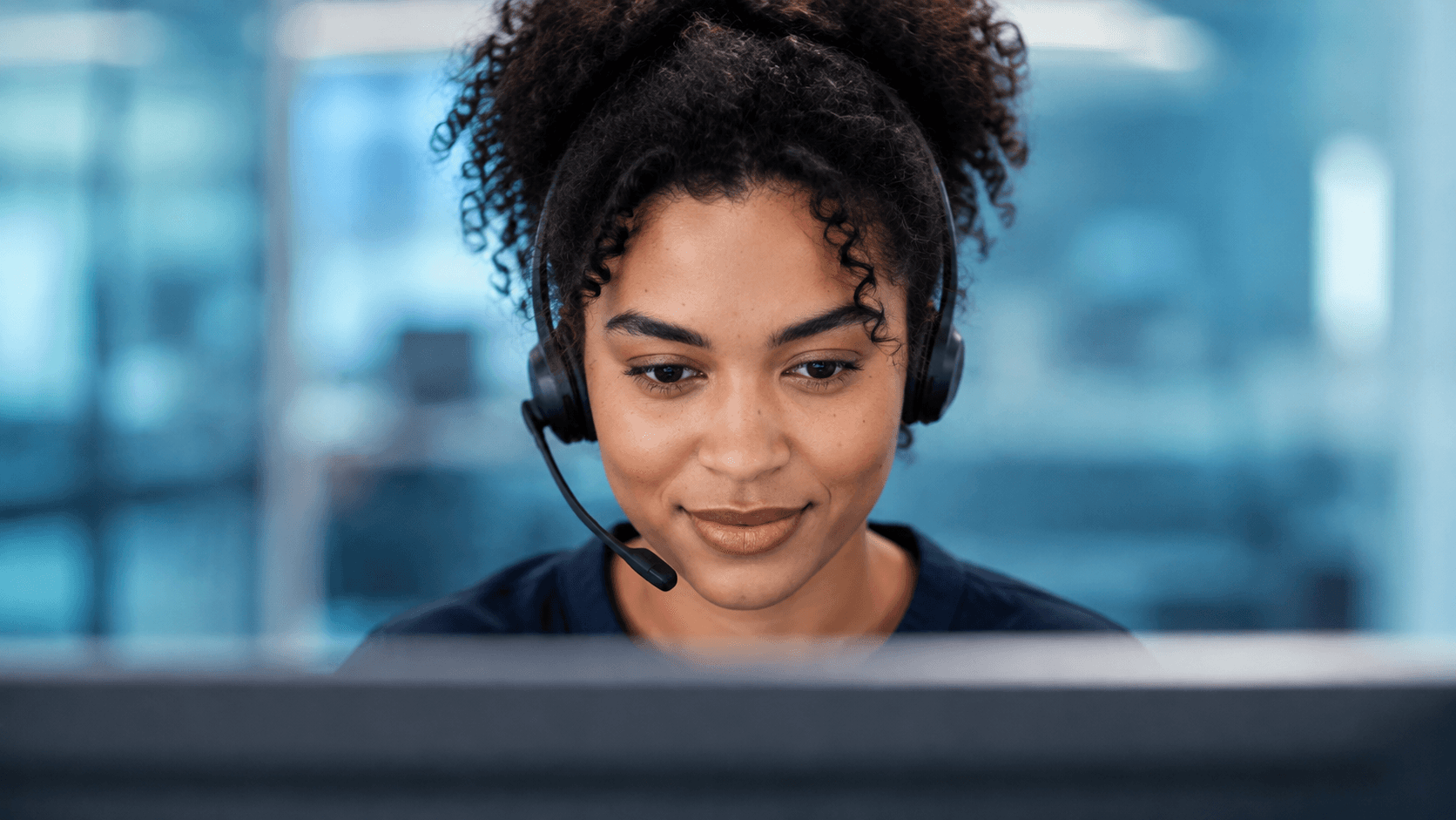 A young female citizen-support advisor wearing a modern headset works at a desktop monitor.