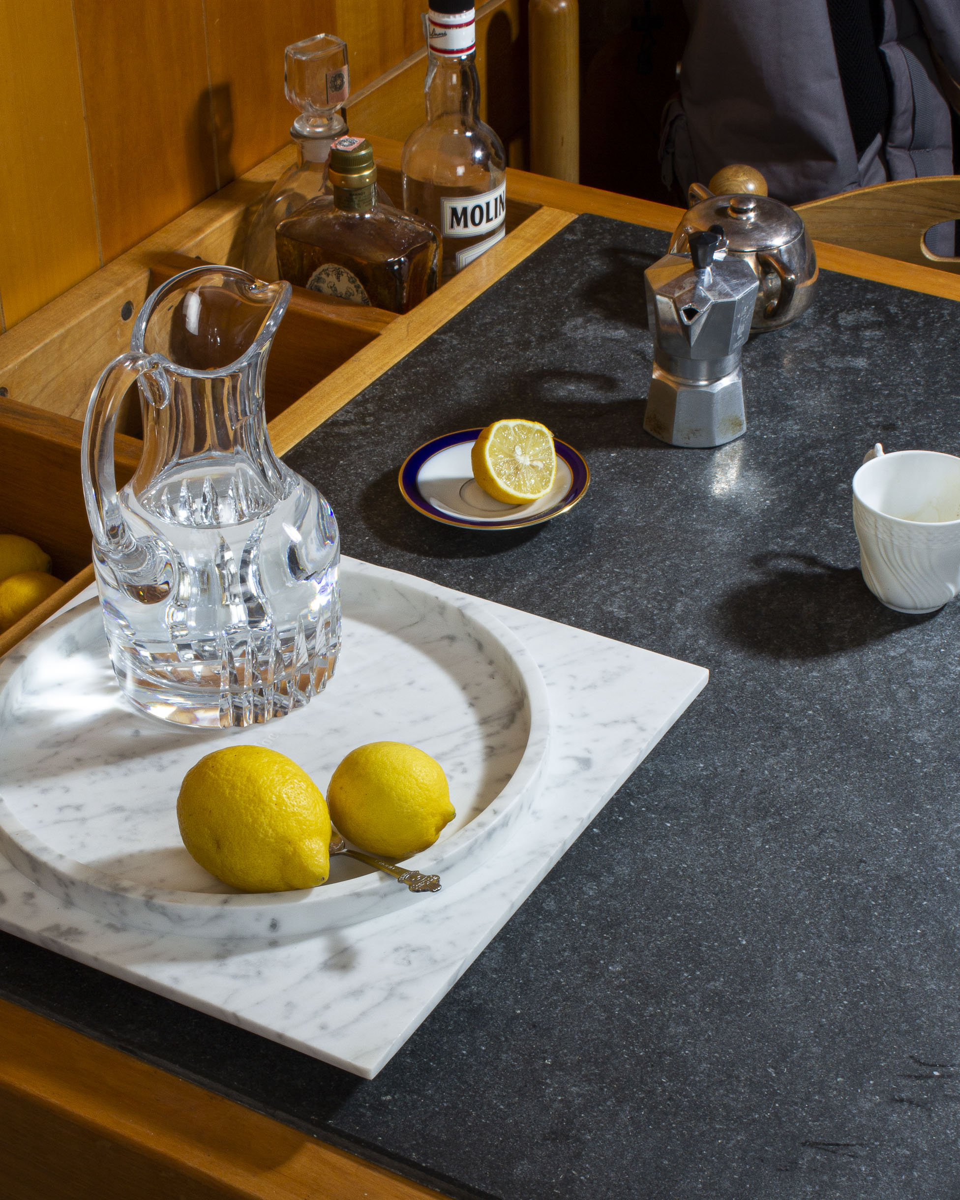 Photo d'une table de cuisine à l'ancienne sur laquelle est posée un plateau en marbre et dans lequel sont posés une carafe d'eau pleine et des citrons