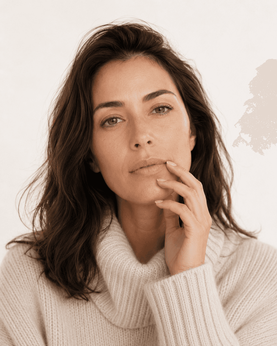 Mulher adulta usando suéter claro de gola alta, com uma das mãos próxima aos lábios e expressão serena, em contexto de inverno