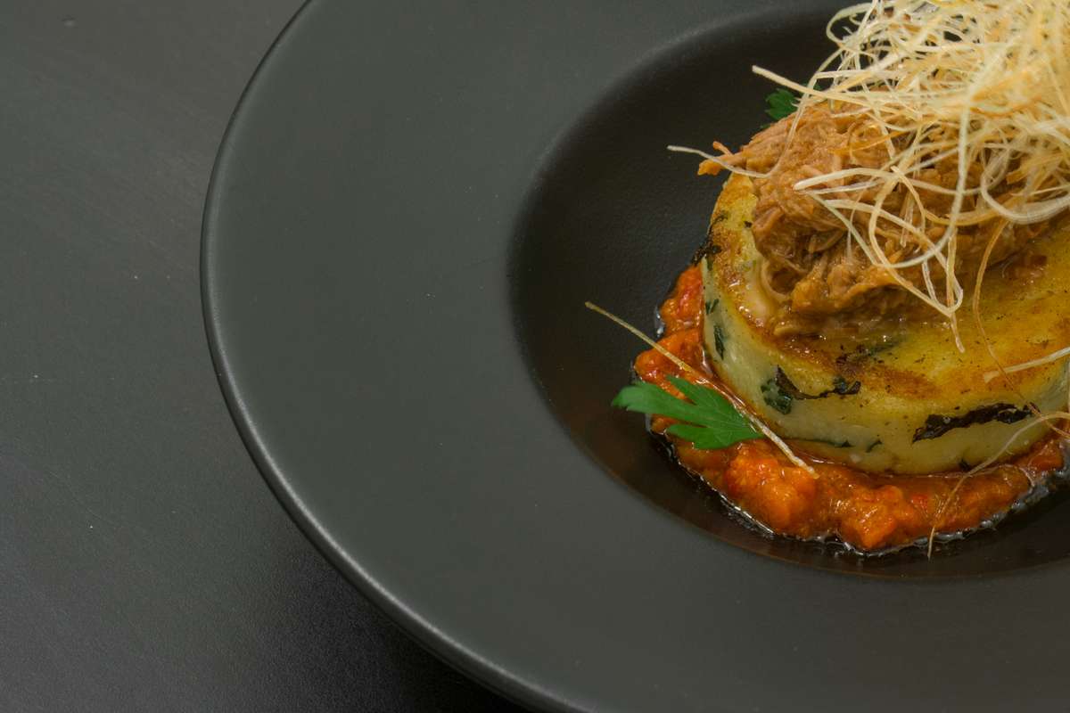 A gourmet layered vegetable stack topped with crispy fried leeks on a large matte black plate.