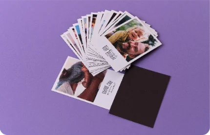 Pessoa segurando foto de casal sorridente em viagem ensolarada, com mesa azul, laranja e suco ao fundo