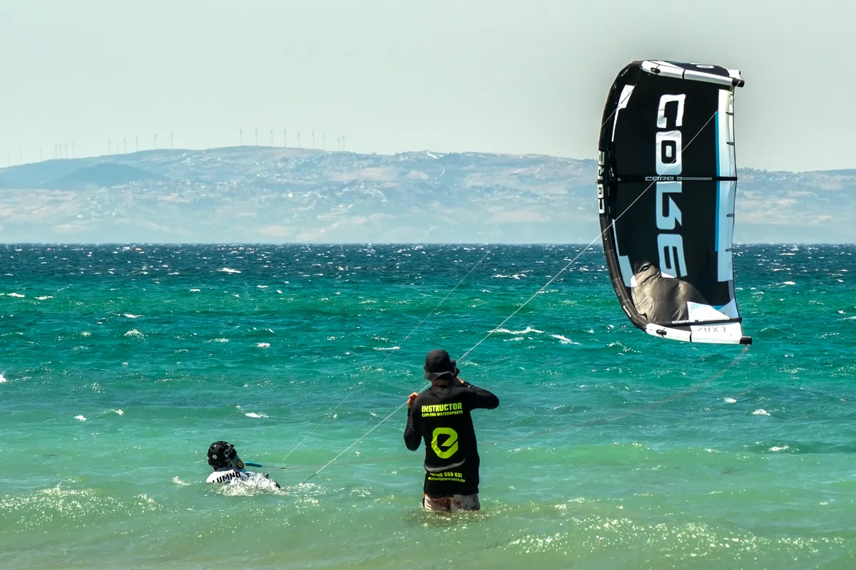 Beginner kitesurf lesson — instructor coaching a student on body drag and waterstart in shallow water — Explora Watersports Tarifa