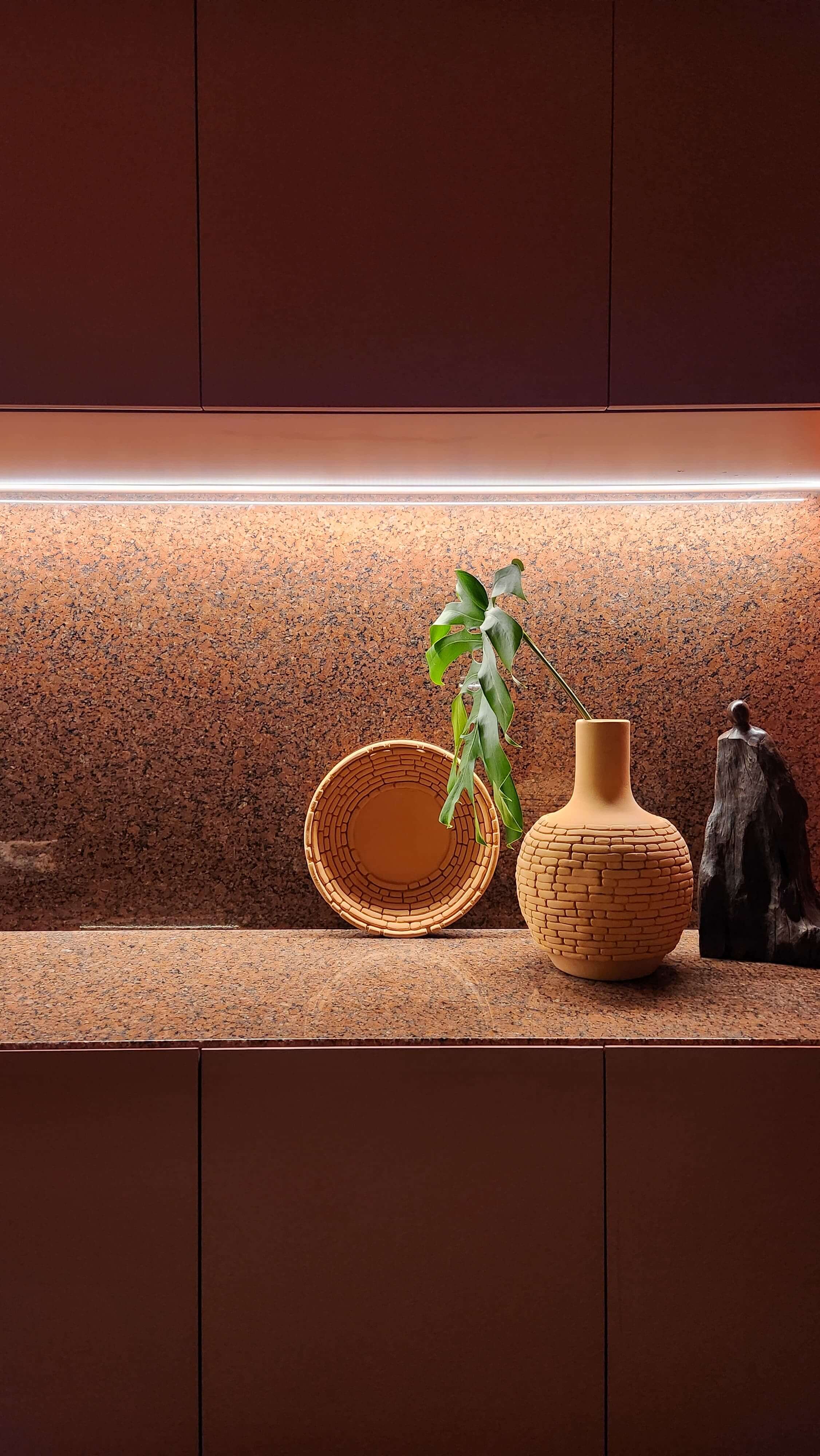 under cabinet lighting in a warm and dark modern kitchen illuminating a countertop set with pottery and a plant