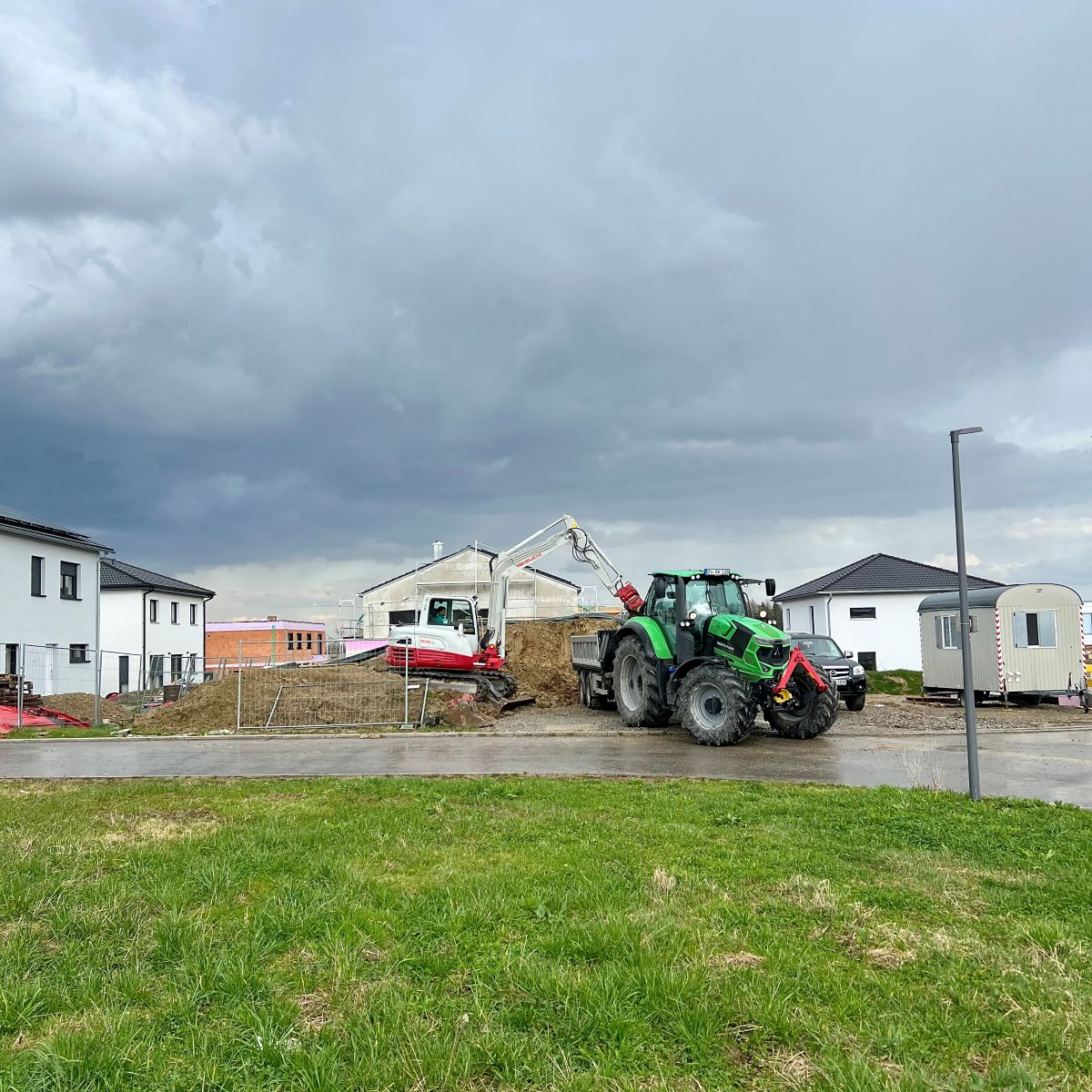 Ansicht einer großen Baustelle mit einem Deutz Traktor im Vordergrund und einem Bagger im Hintergrund bei Erdarbeiten zur Geländemodellierung.