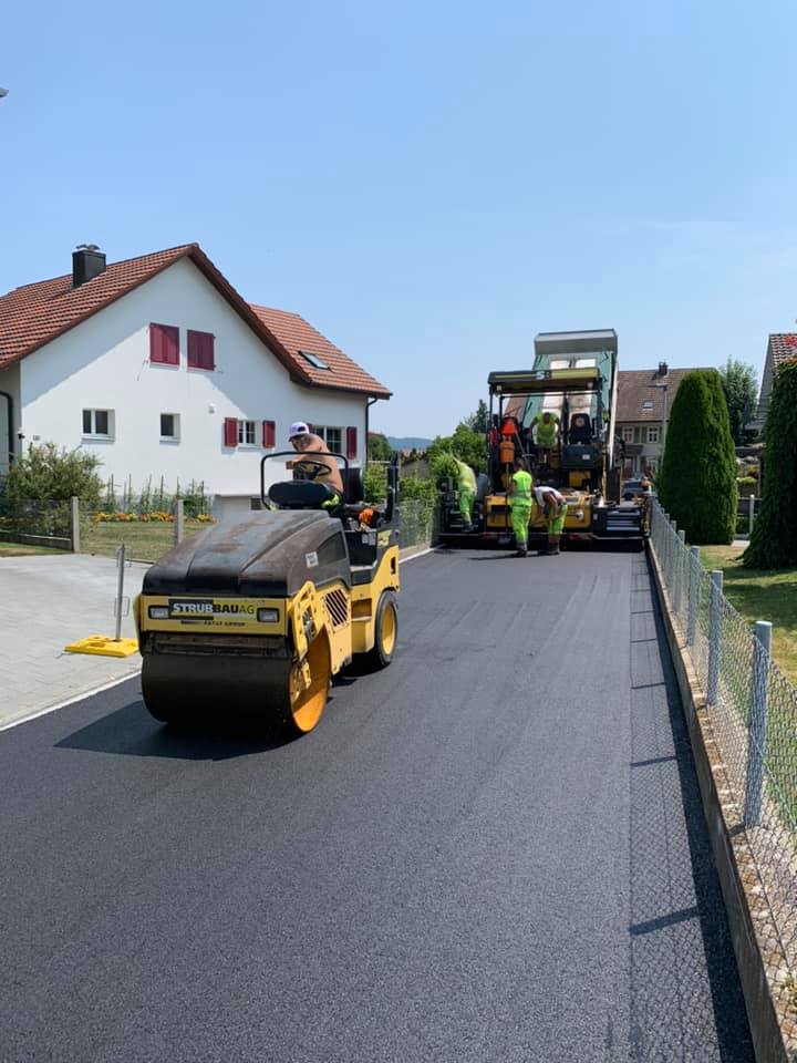 Fresh asphalt paving by Strub Bau AG on a residential street using roller compactor and paver – high-quality road construction in Switzerland.