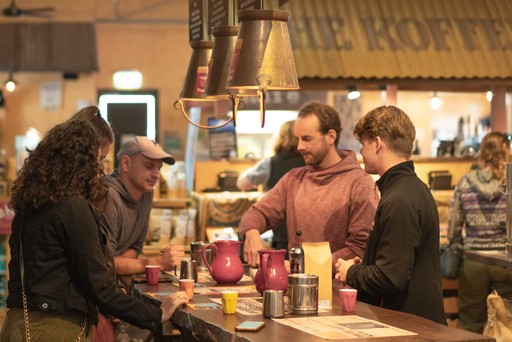 Guide leading a coffee tasting at a local roasting house, at a high table with the roastery in the background
