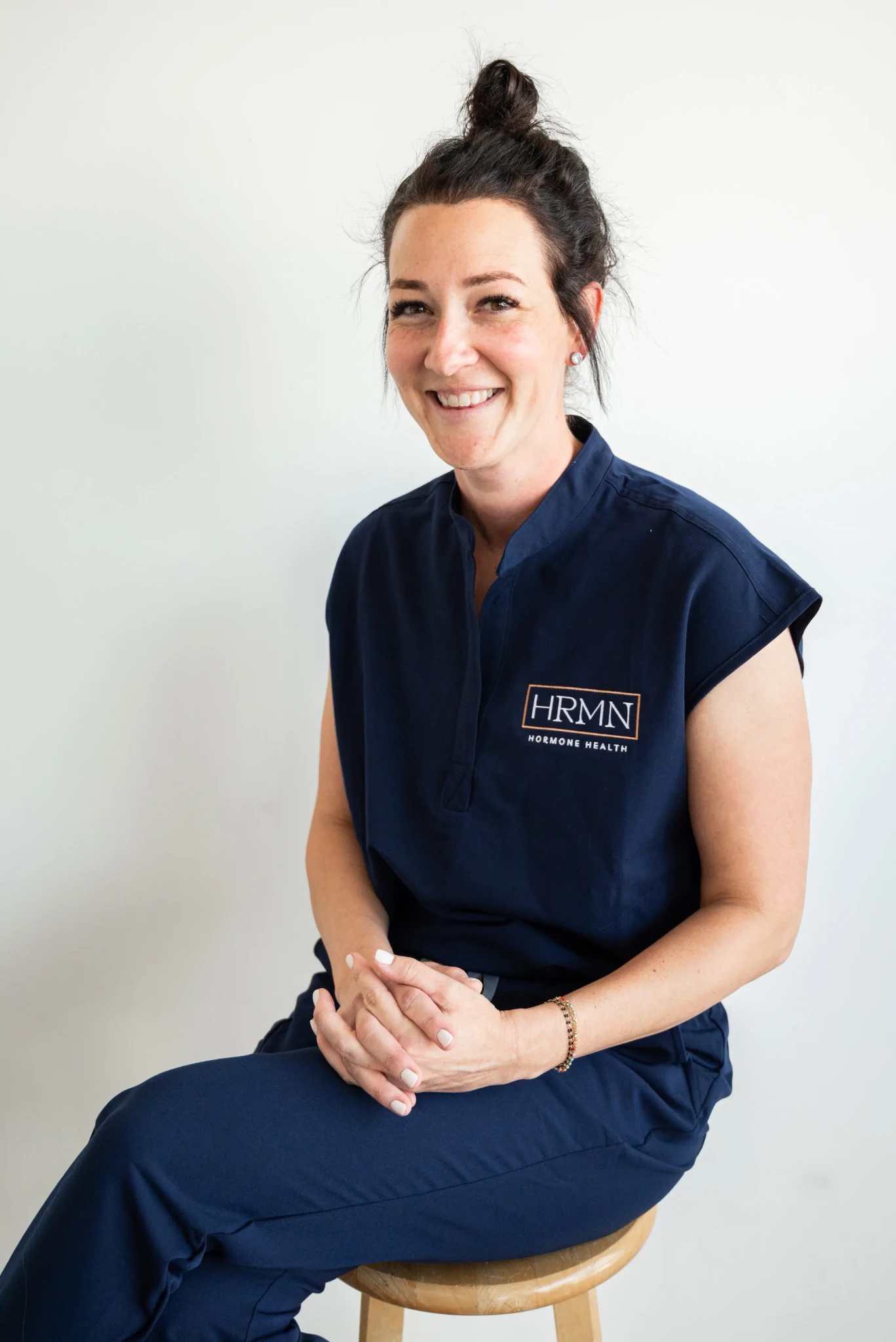 Portrait of Jamie Ruiz, a certified Physician Associate, smiling in a professional medical setting with shelves of supplements and medical products in the background.