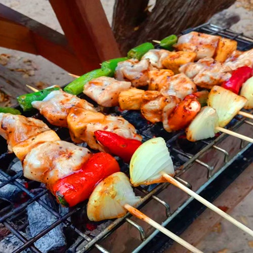 在炽热的煤火上,金属架正烤着用腌制鸡肉、甜椒和洋葱串成的串烧。