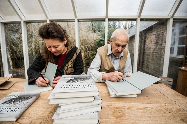 Suzi og Heinrich underskriver kopier af Fra Vestkysten til Østfronten, mens de sidder i udestuen