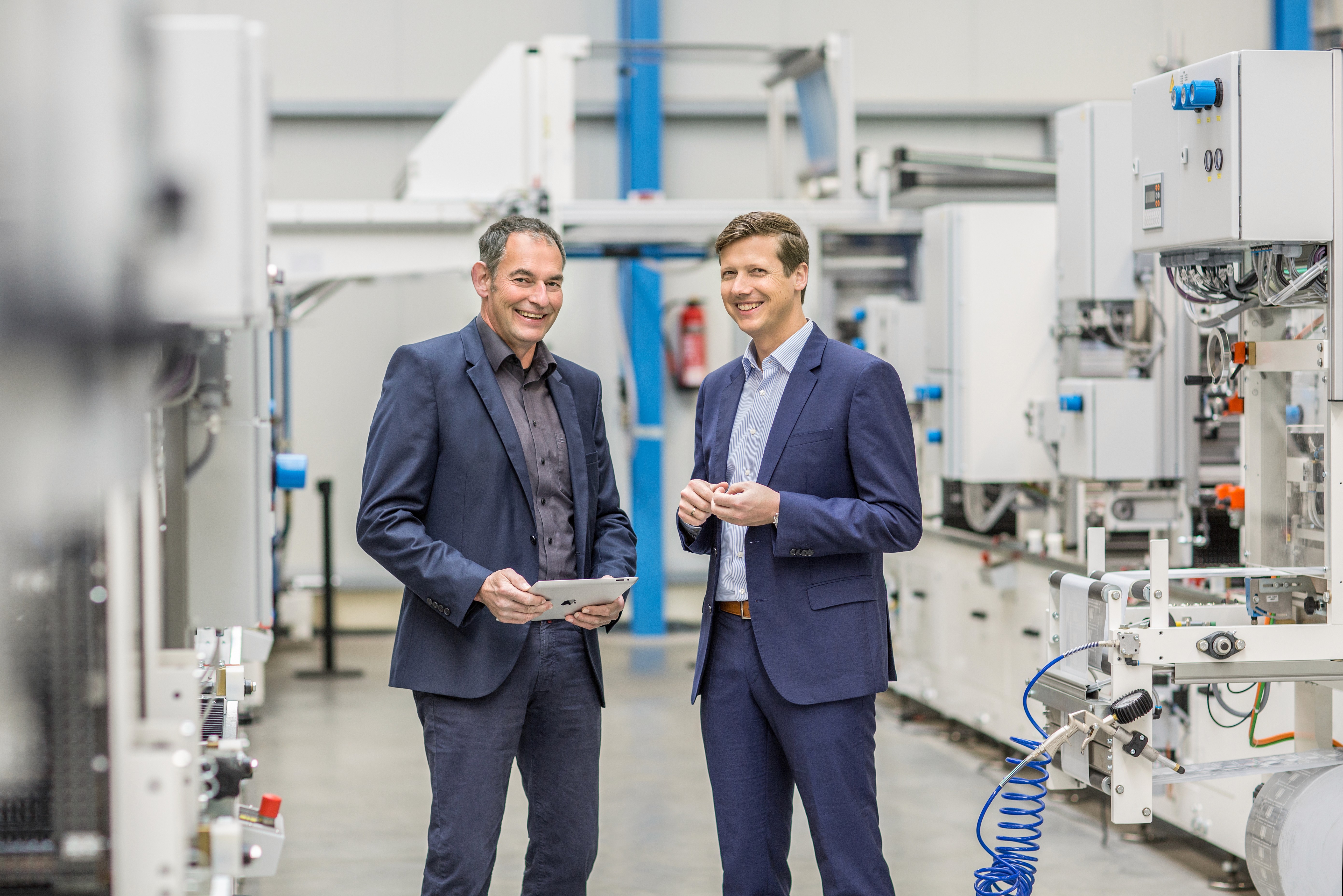 Zwei Manager in Fabrikhalle. Geschäftsleute besprechen Produktion mit Tablet. Industriearbeitsplatz.