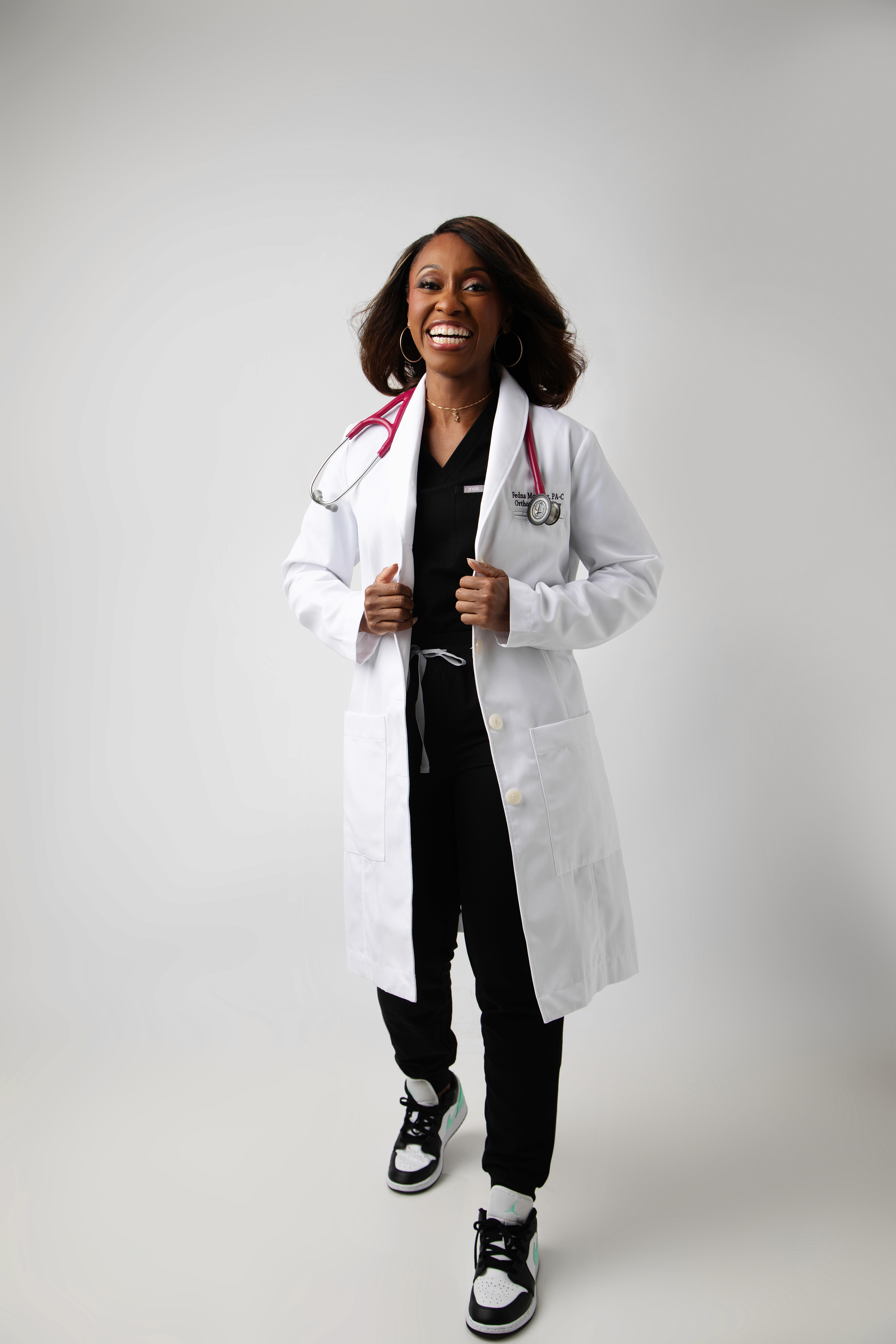 Smiling female therapist with short gray hair, wearing a brown top and a purple shawl, surrounded by a cozy background.
