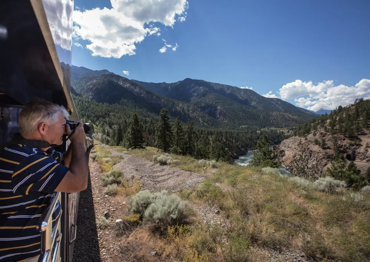 A guest photographing the mountains from the GoldLeaf outdoor viewing platform on the Rocky Mountaineer, Journey Through the Clouds route