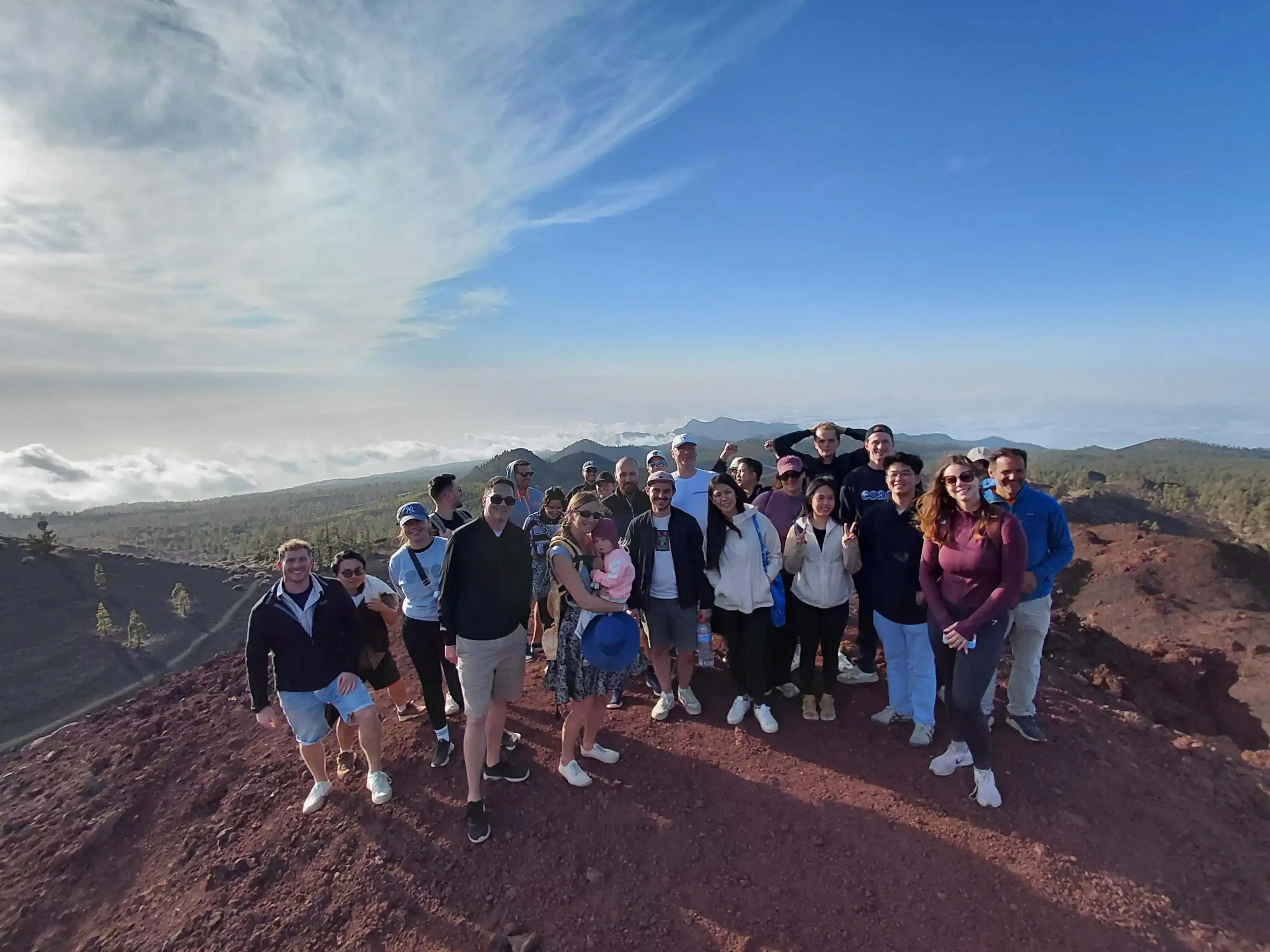Group of people standing on a mountain summit with scenic clouds and forest in the background