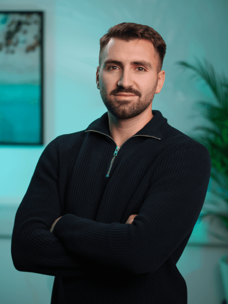 A woman with short curly hair wearing a black t-shirt looks into the camera.