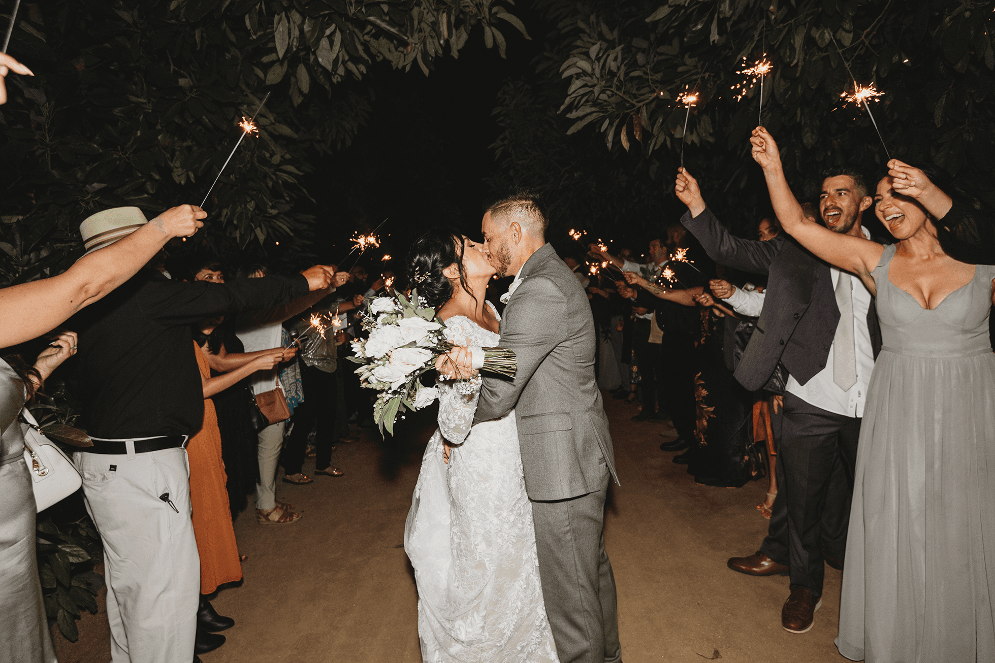 Bride and groom kissing in sparkler tunnel at night
