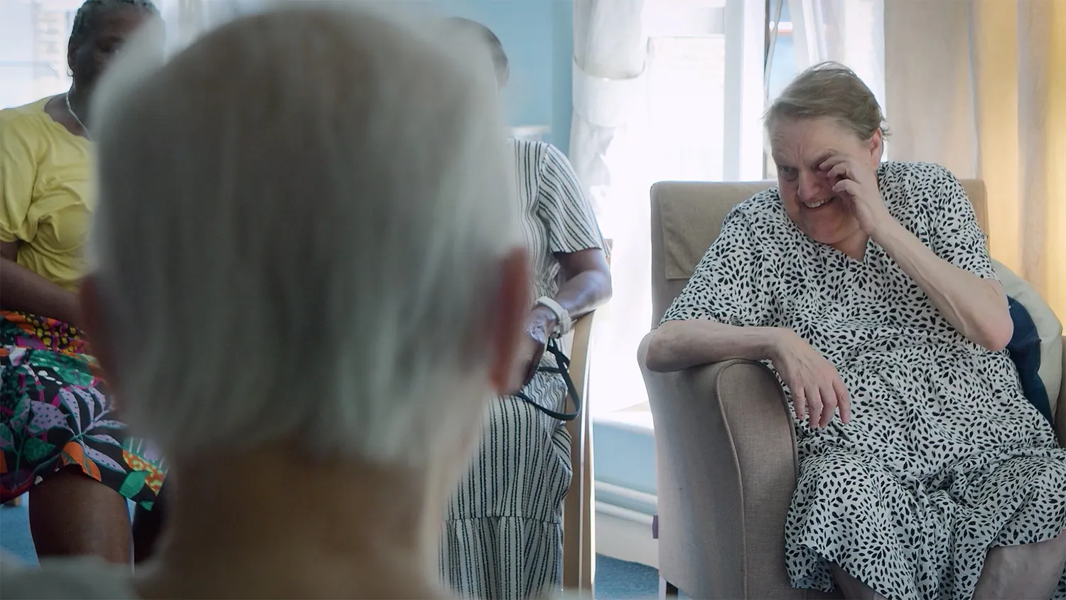 Older woman smiling during a group activity in a bright communal room.