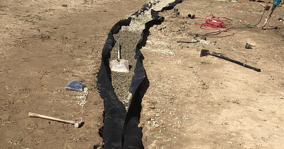 Drainage trench in a Roseville yard lined with filter fabric and filled with drain rock, shovel set in the run.