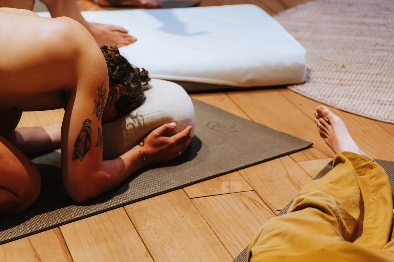 Man met tatoeages ligt voorovergebogen met zijn hoofd op een kussen op een yogamat