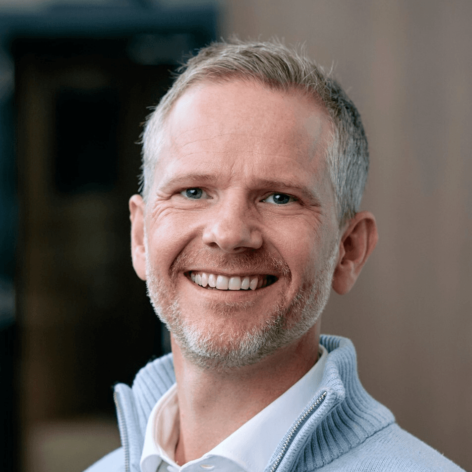 A confident person with short, styled hair and a leather jacket poses against a dark backdrop.