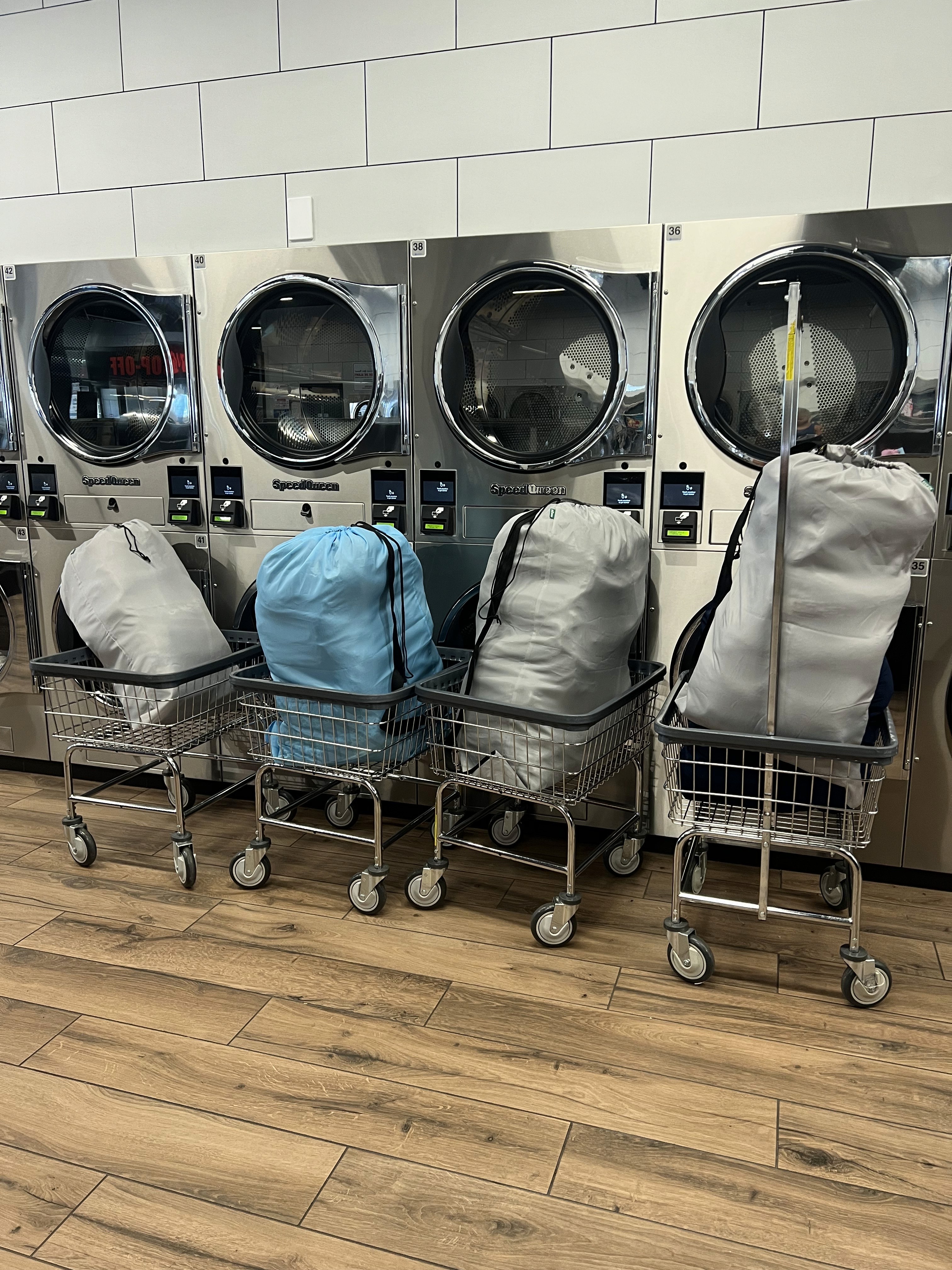 Laundry carts filled with large branded delivery bags at a commercial laundromat in Brooklyn, prepared for customer pickup and delivery.