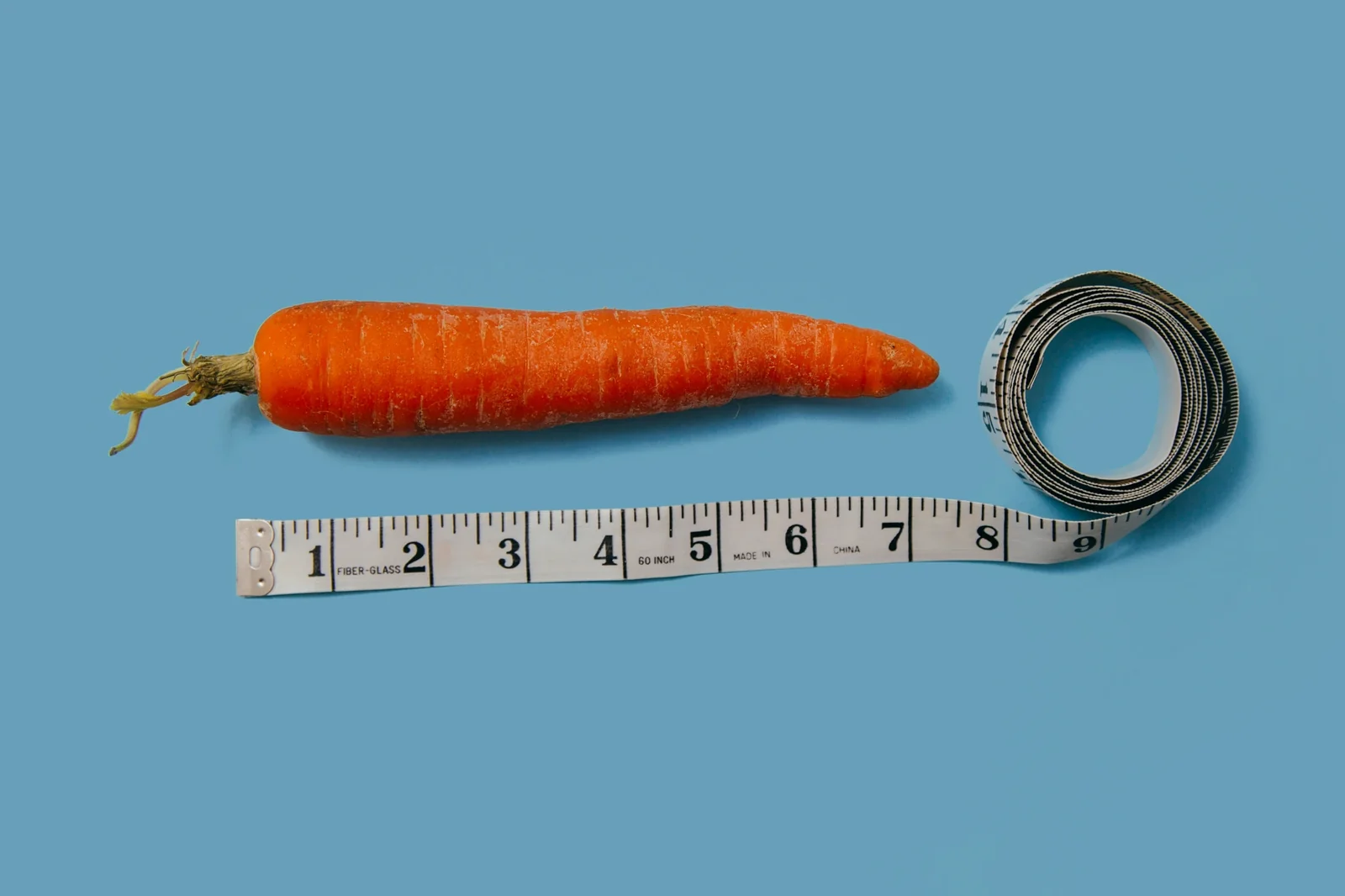 A carrot measured with a tape measure against a blue background, symbolizing measurement and metrics.