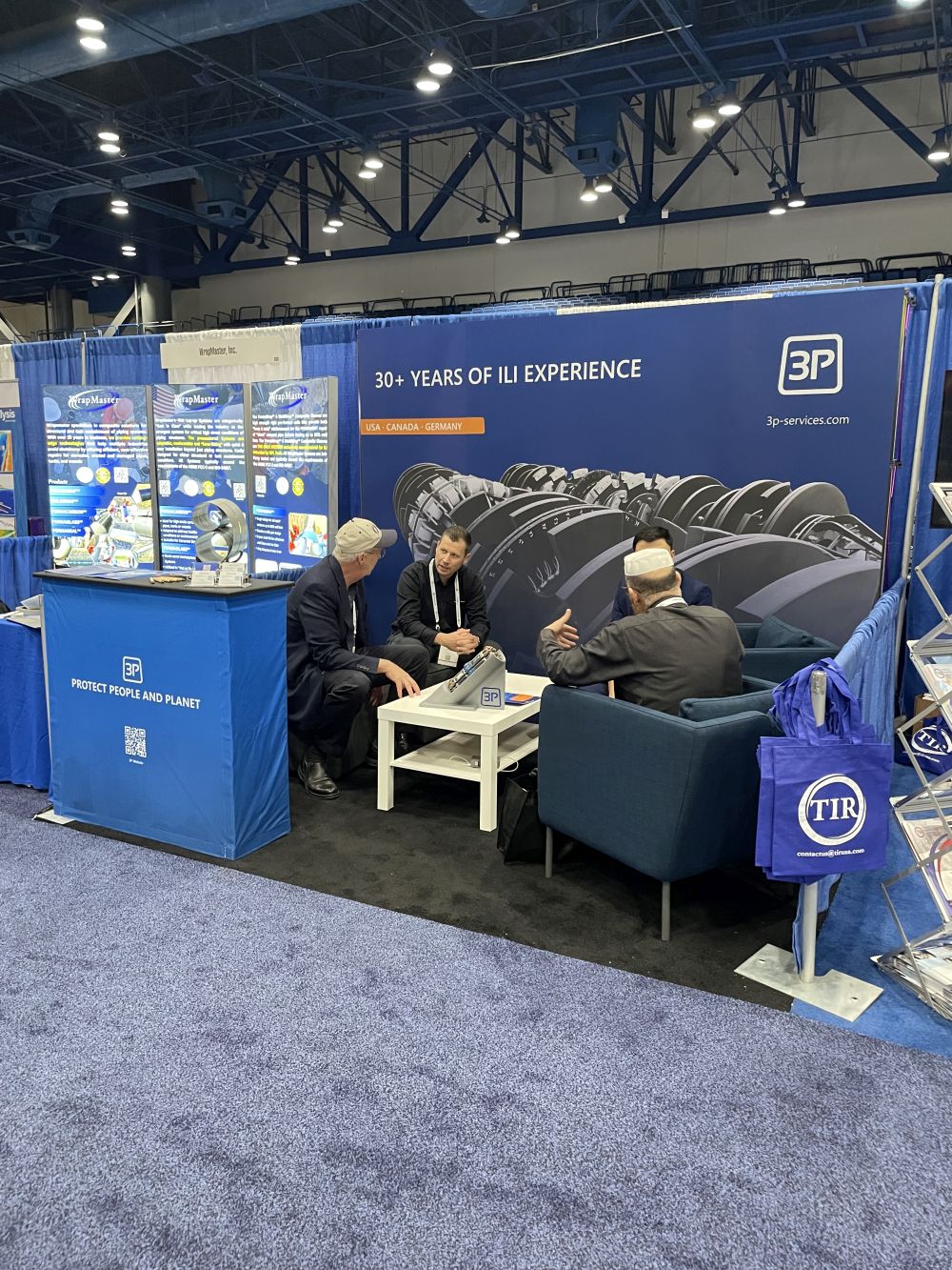 Attendees sit at a booth promoting 30+ years of IJJ experience. Booth includes signage, product images, and brochures.