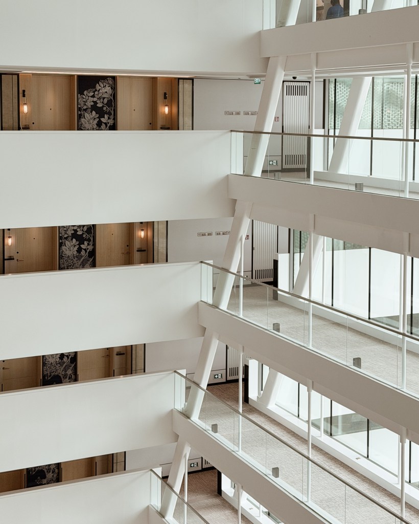 Interior view of a modern building showcasing multiple floors with glass railings and decorative wall panels near rooms.