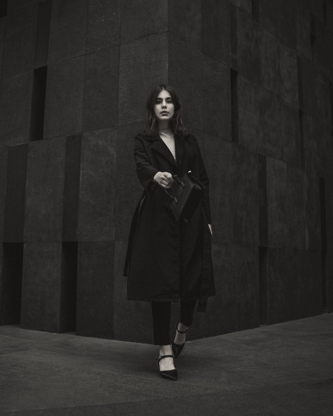 Model walking out of dark stone in a black wrap coat