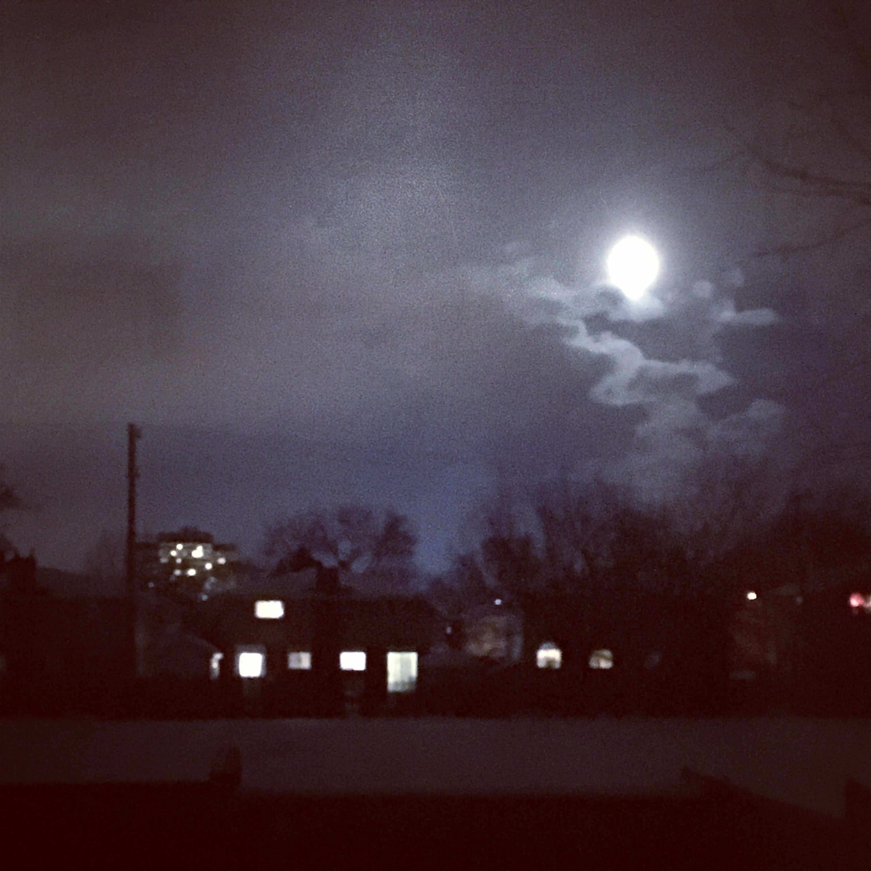 A fuzzy night sky, with lights glowing in homes, and the moon shining bright above. Photo by Rafia Mahli.