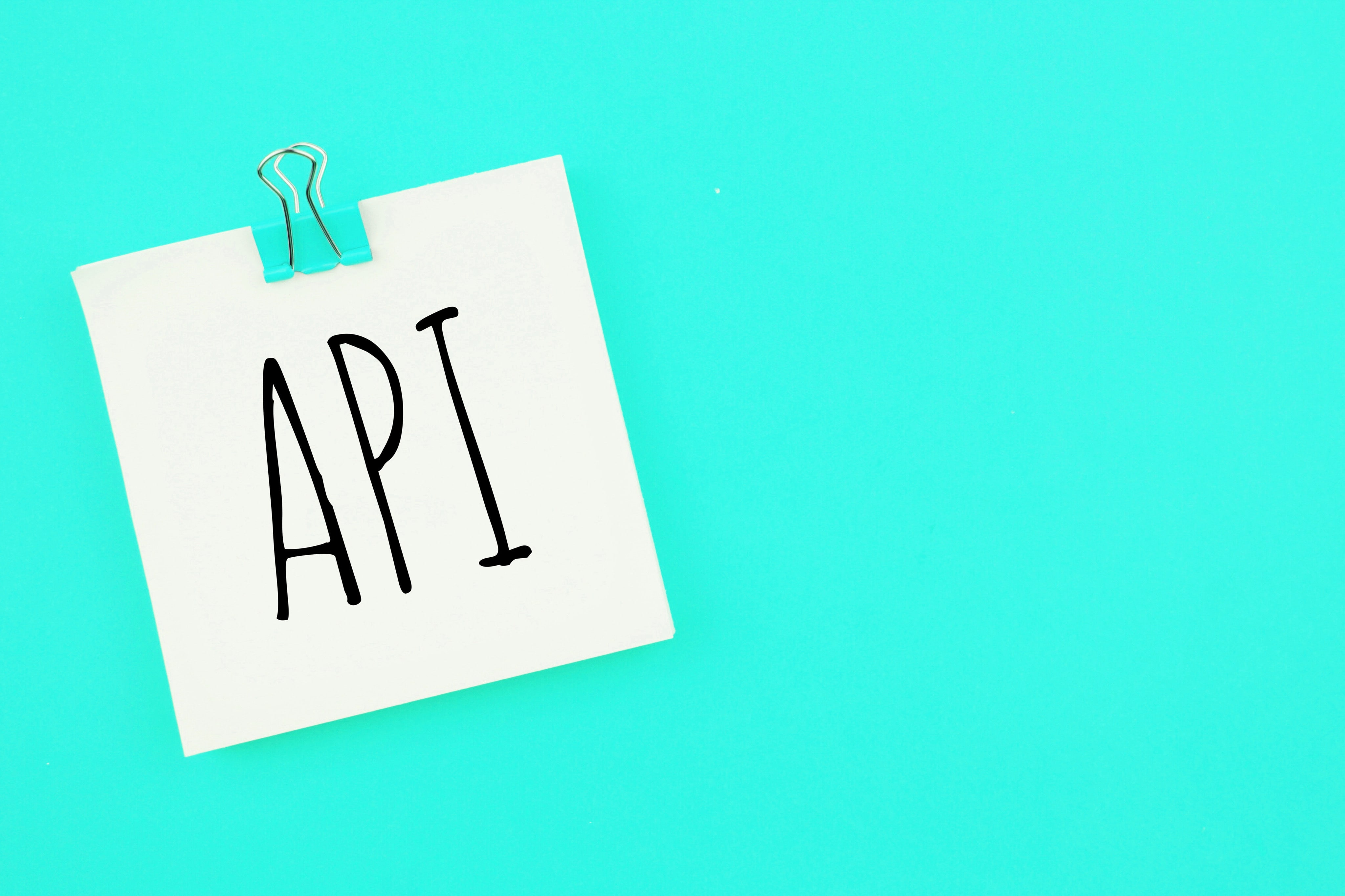 Sticky note with the word 'API' clipped to a turquoise background, symbolizing software integration or development.
