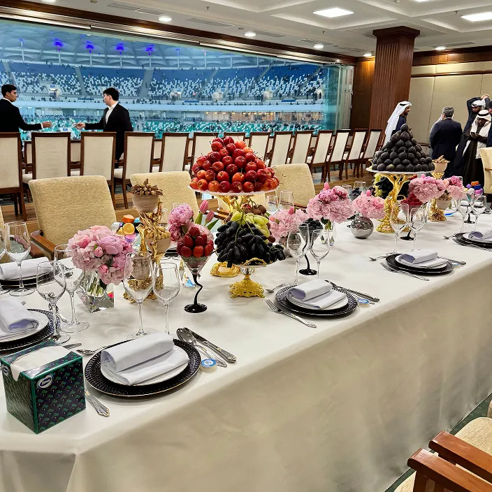 Lavish dining table with ornate flower and fruit centerpieces, elegant tableware, and formal seating in a luxurious event space with aquatic-themed decor.
