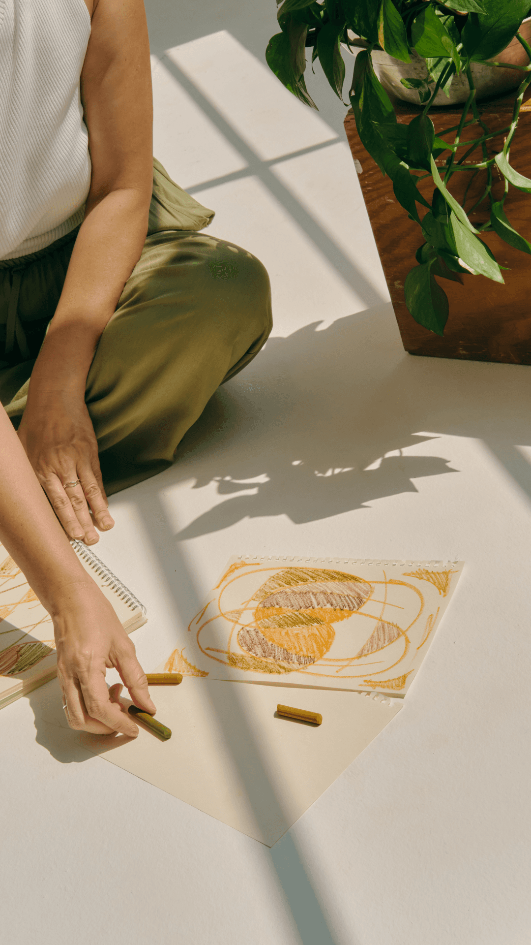 Girl sitting on the floor, drawing with orange and brown crayons on white paper, symbolizing the importance of mindfulness in mental and emotional wellbeing.