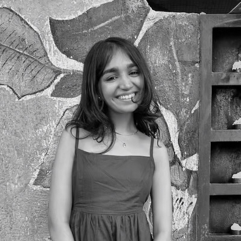 A portrait of Anushri Shah Riddhish, a student from Mumbai, India, belonging to the class of 2027. She is smiling and dressed in casual attire, with a background that suggests an academic or social setting.