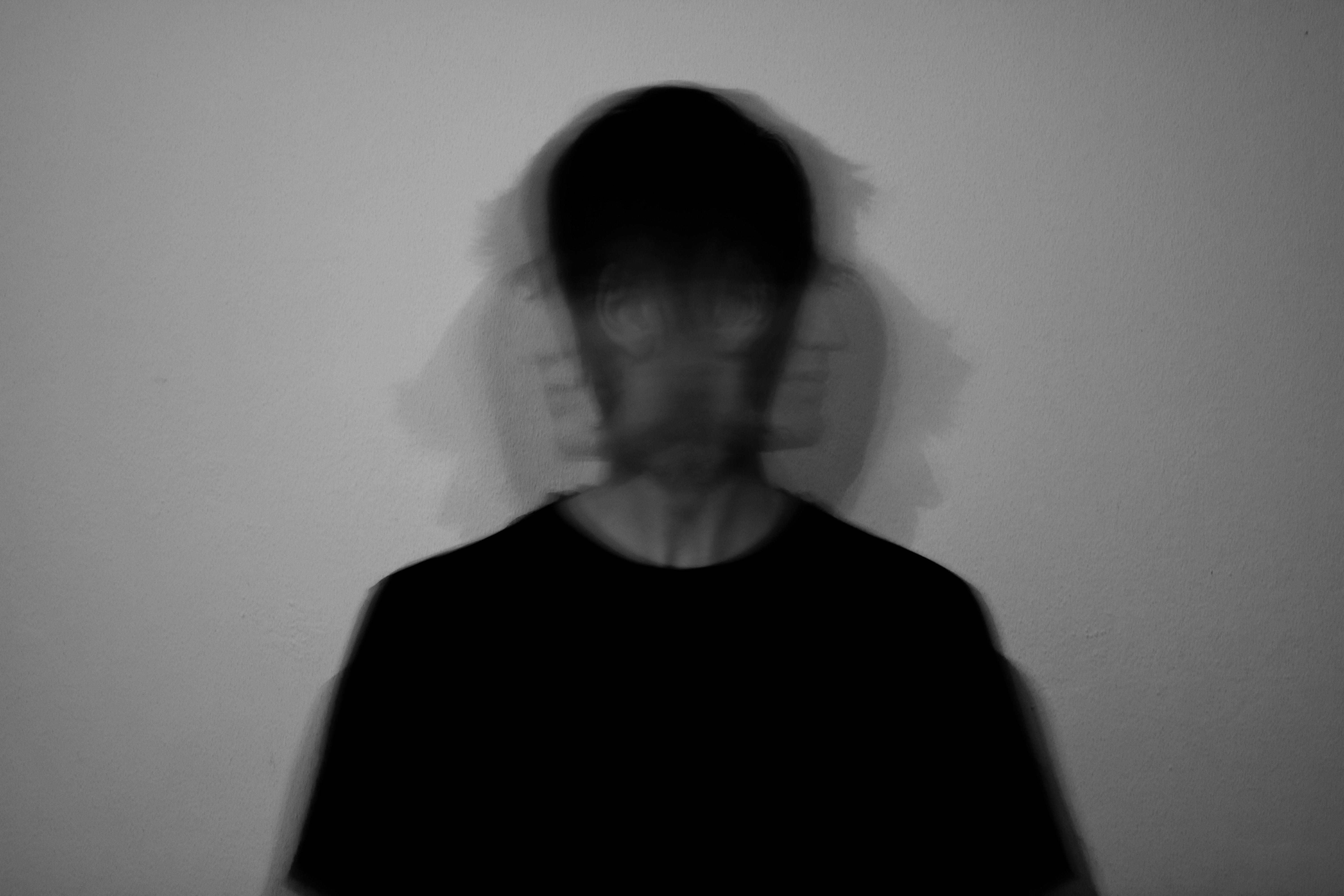 Man sitting in a dimly lit room, wearing a beige shirt and looking contemplative.