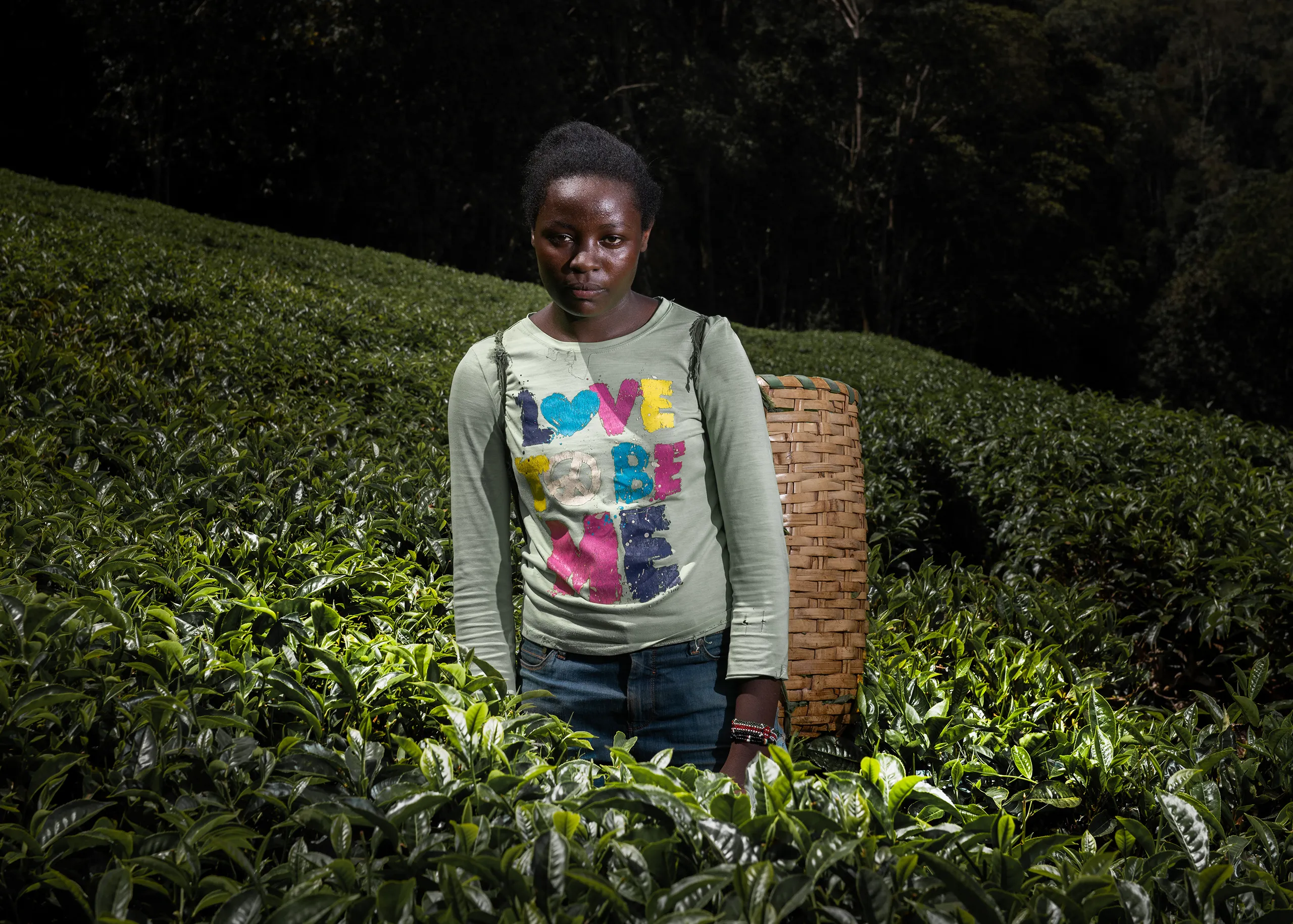 Candid portrait of a young female Kenyan worker in a black and white striped shirt within a tea field.