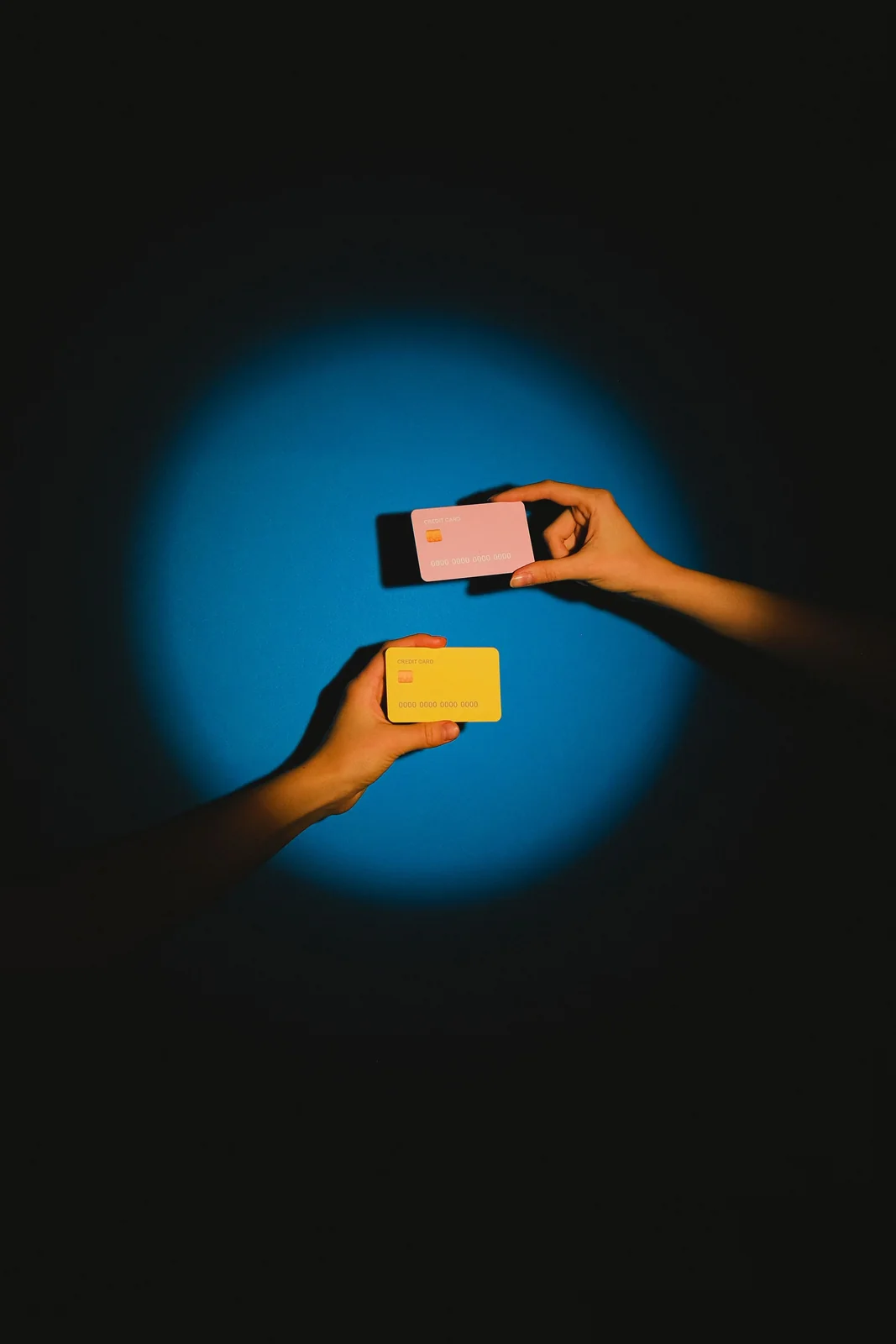 Two hands hold generic colorful payment cards against a blue background.