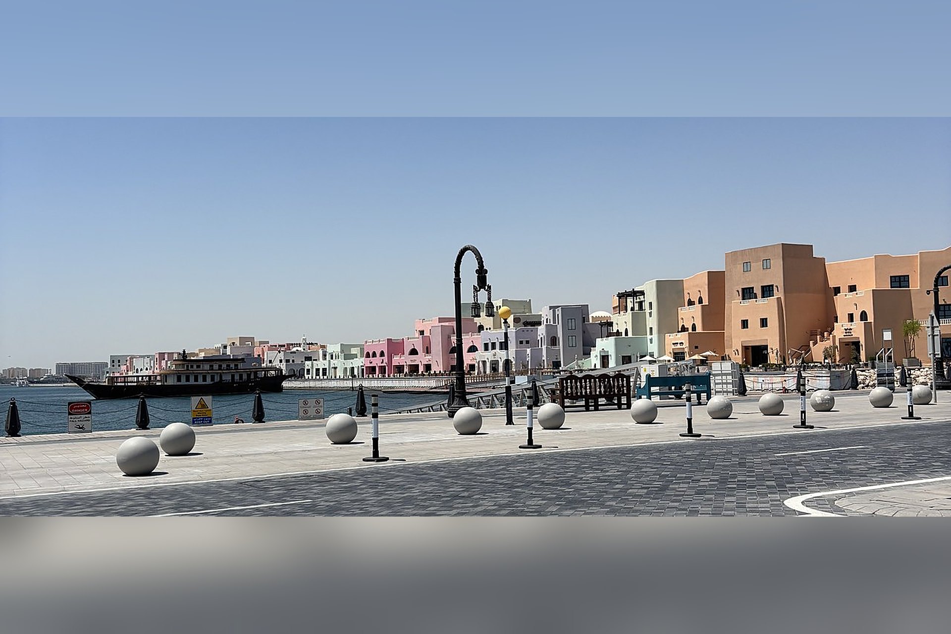 Les façades pastel du Mina District, le vieux port de Doha, avec un boutre amarré devant le quai : la promenade du bord de l'eau y est rafraîchie sur plus de 530 mètres